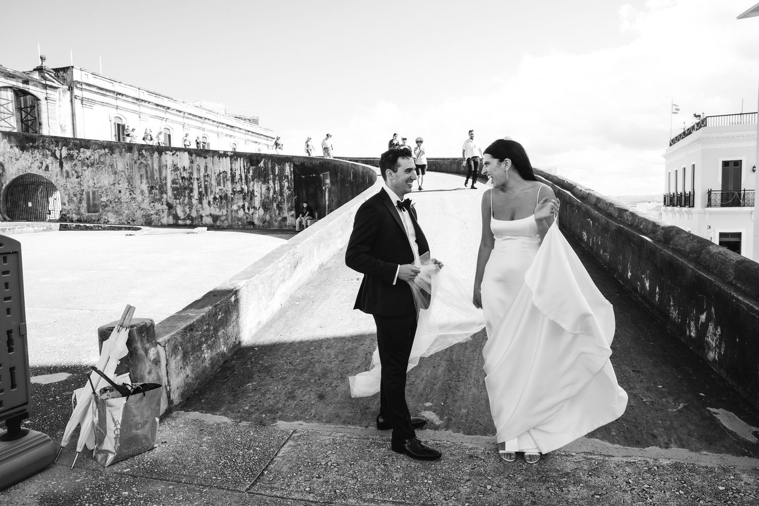 A black and white collage of six romantic wedding photos taken along a seawall showing the bridal couple in various poses.