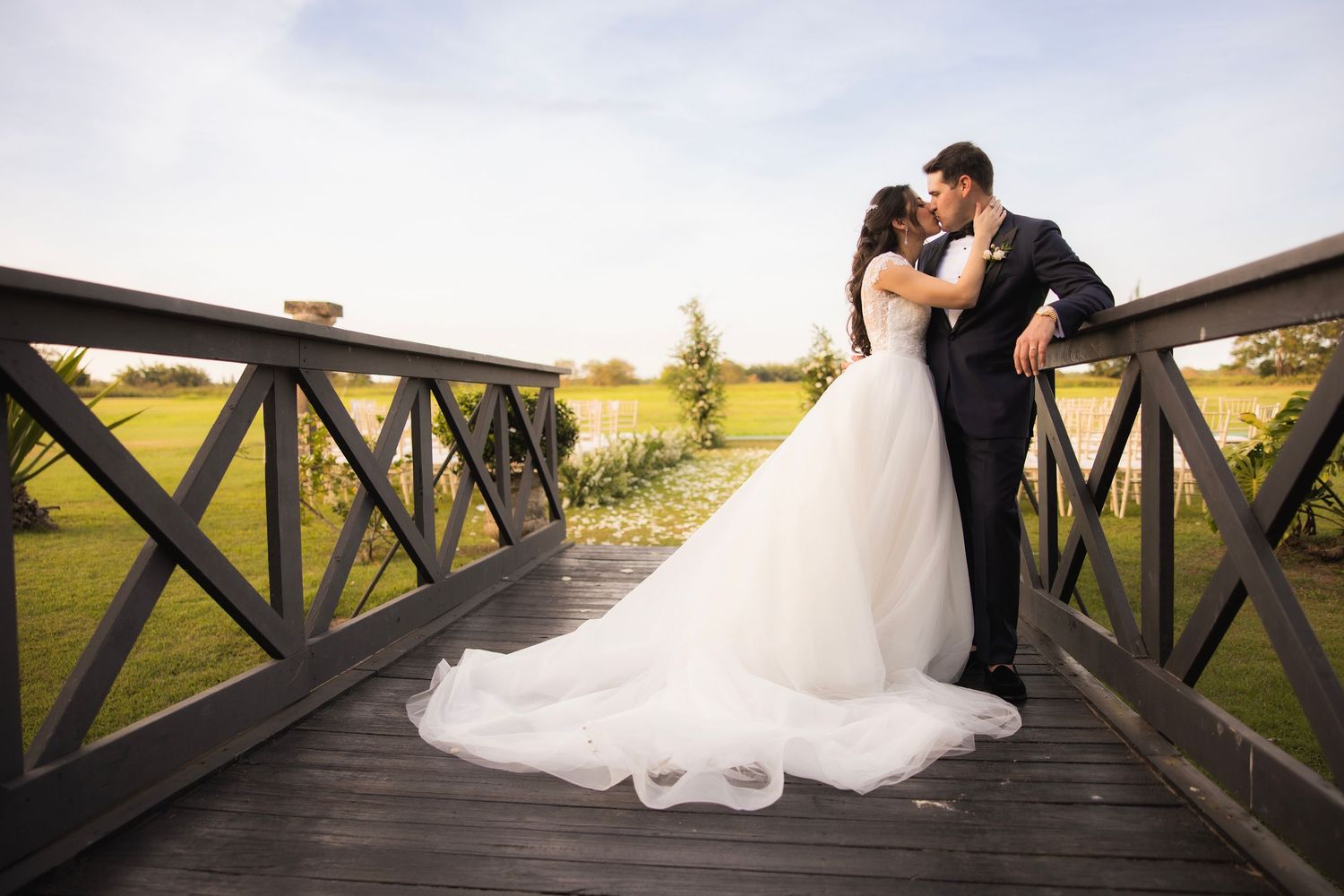 Romantic wedding couple posing on wooden bridge against countryside landscape.