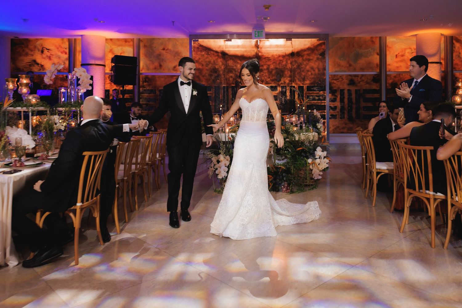 A romantic wedding reception venue with warm lighting, floral centerpieces, and elegant table settings in a ballroom setting.