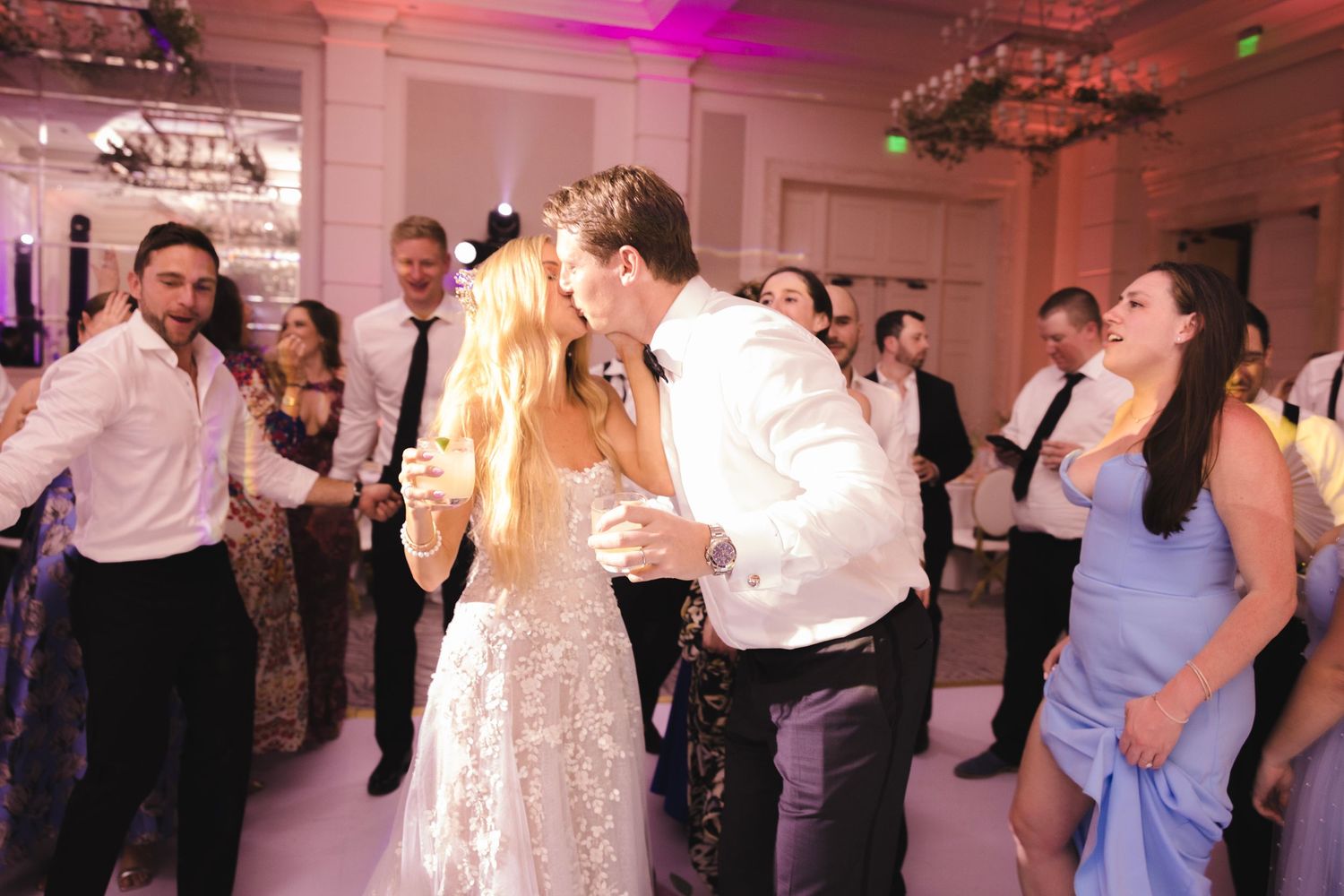 Wedding celebration on the dance floor with guests enjoying lively dancing under purple mood lighting.