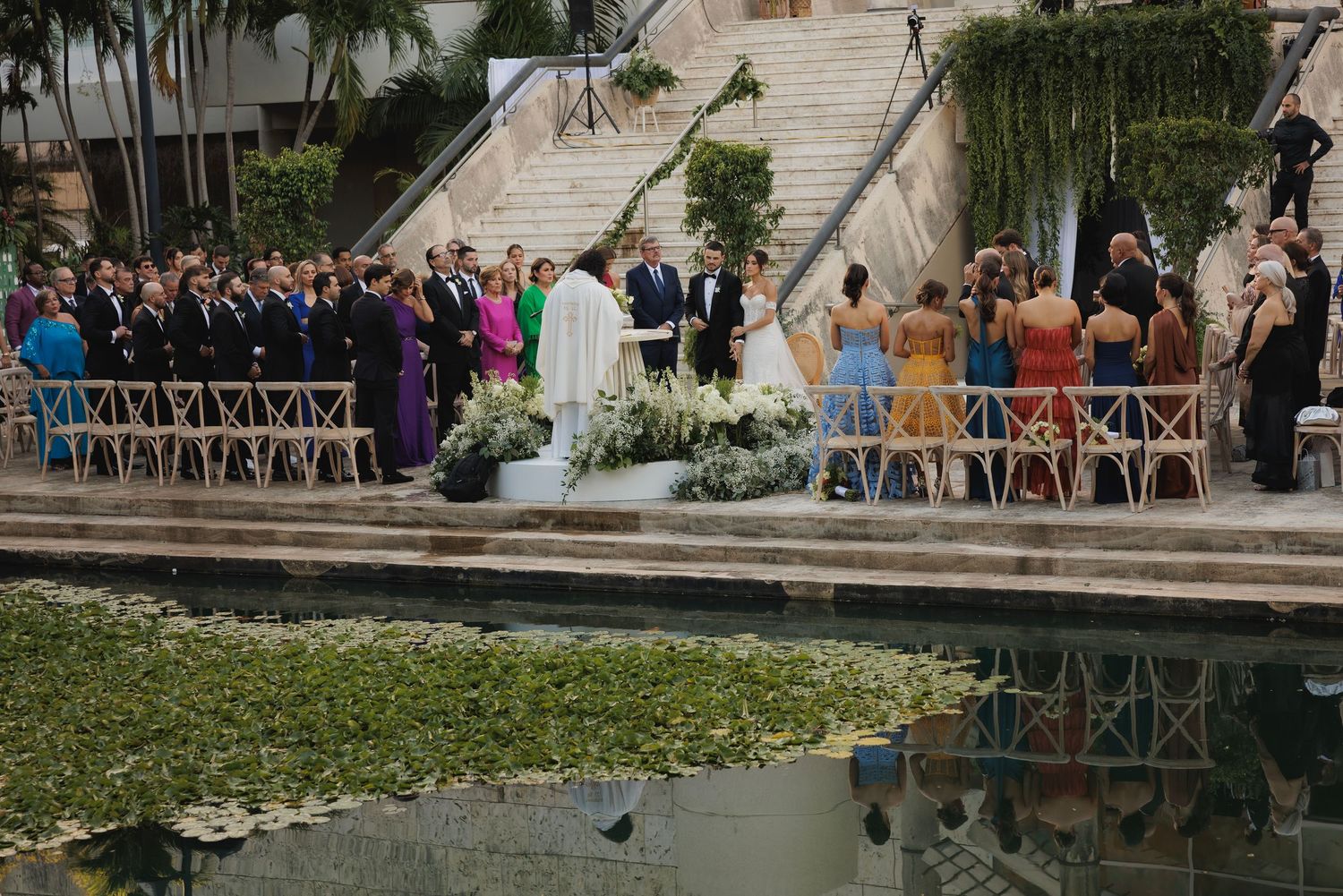 Panoramic view of wedding guests gathered at an elegant outdoor venue with stone architecture.