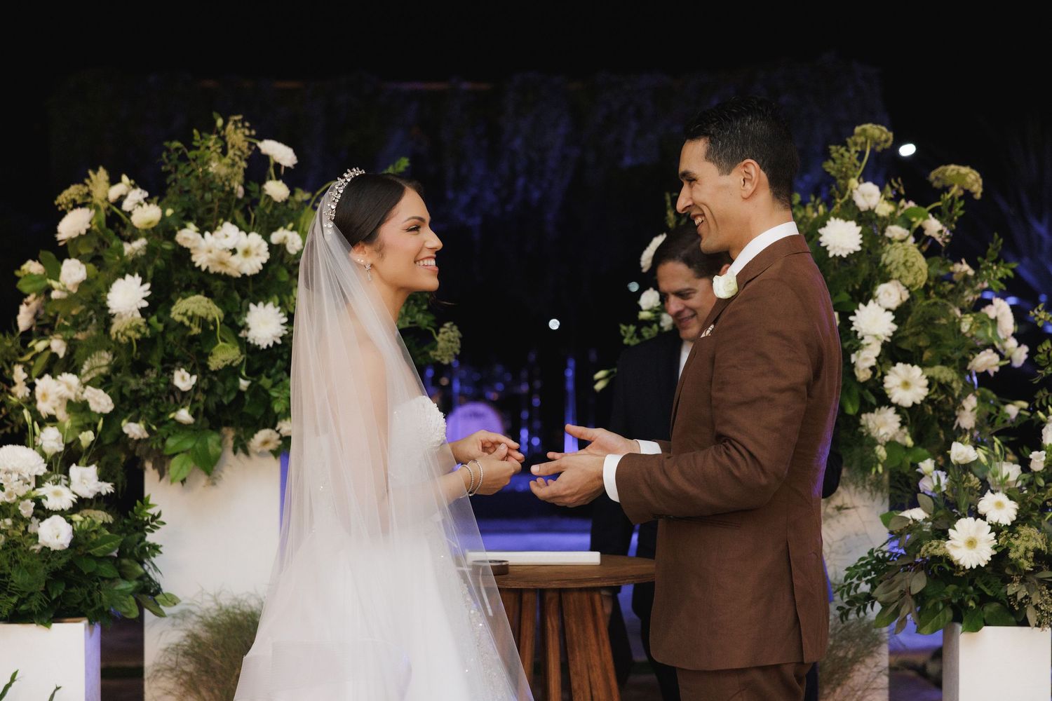 Wedding ceremony with floral arch featuring white and blue flowers as couple exchanges rings.