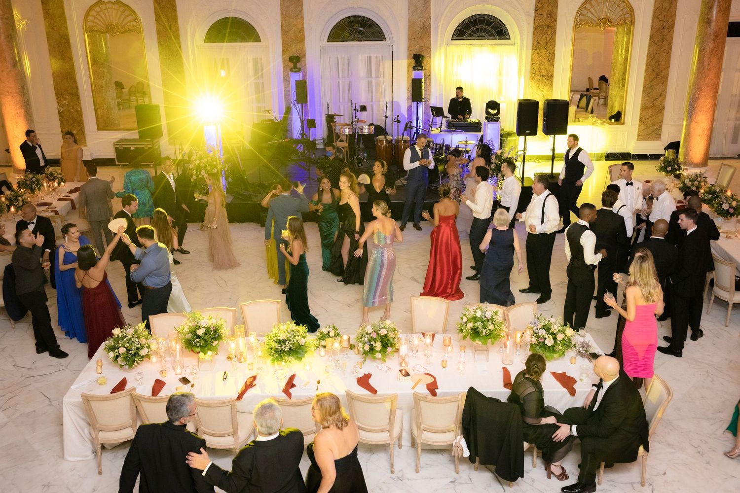 Wedding reception guests dance together at an elegant venue with soft lighting and glowing chandeliers.