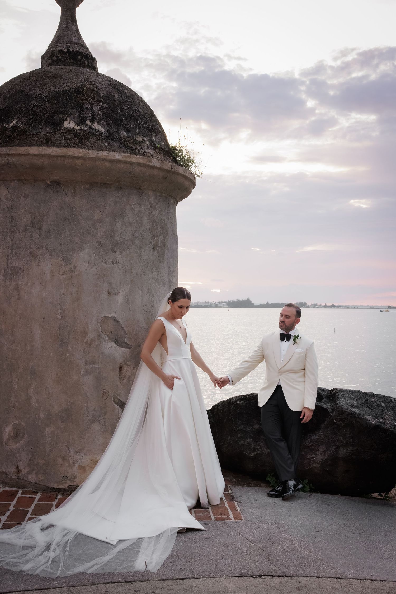 A romantic wedding portrait at sunset by a historic stone garita overlooking the ocean.