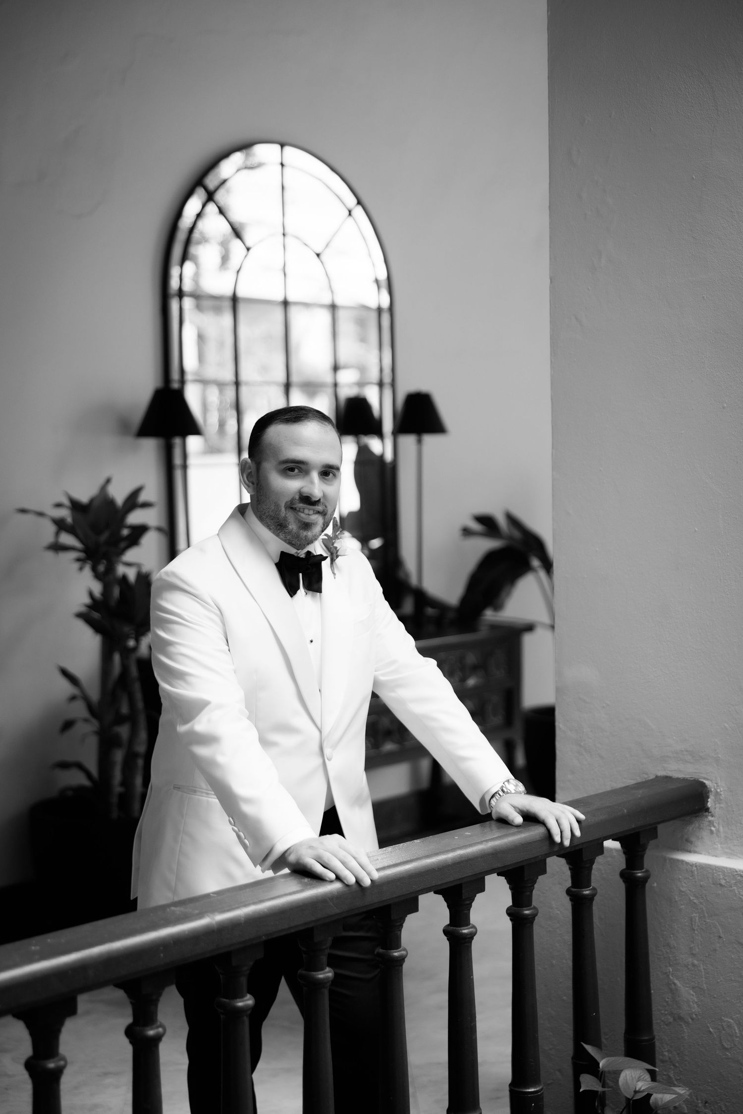 A black and white photo series showing a person in a white suit leaning on a railing in an elegant interior space.