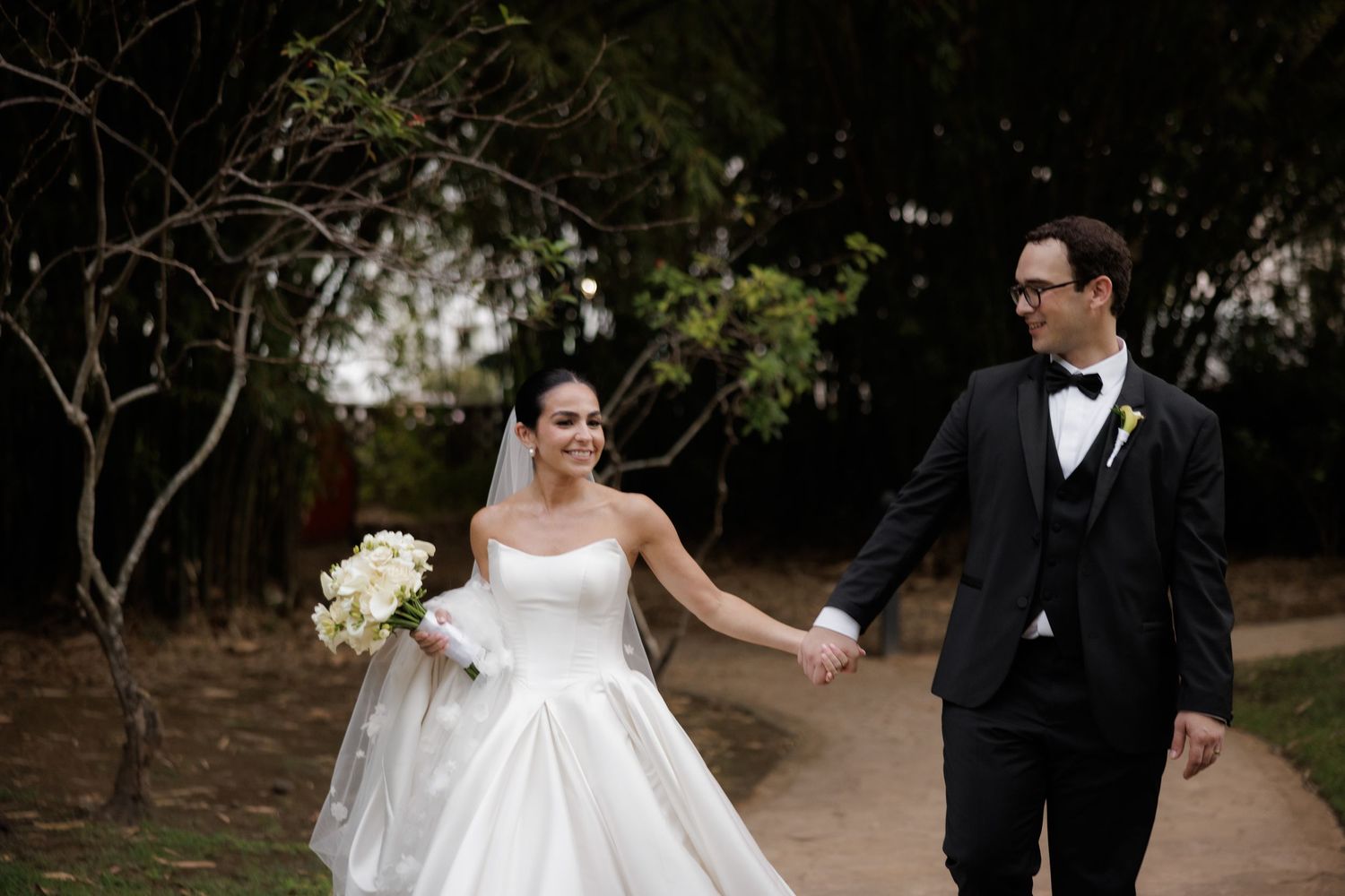 Bride and groom share an intimate moment while walking along a tree-lined path at sunset.