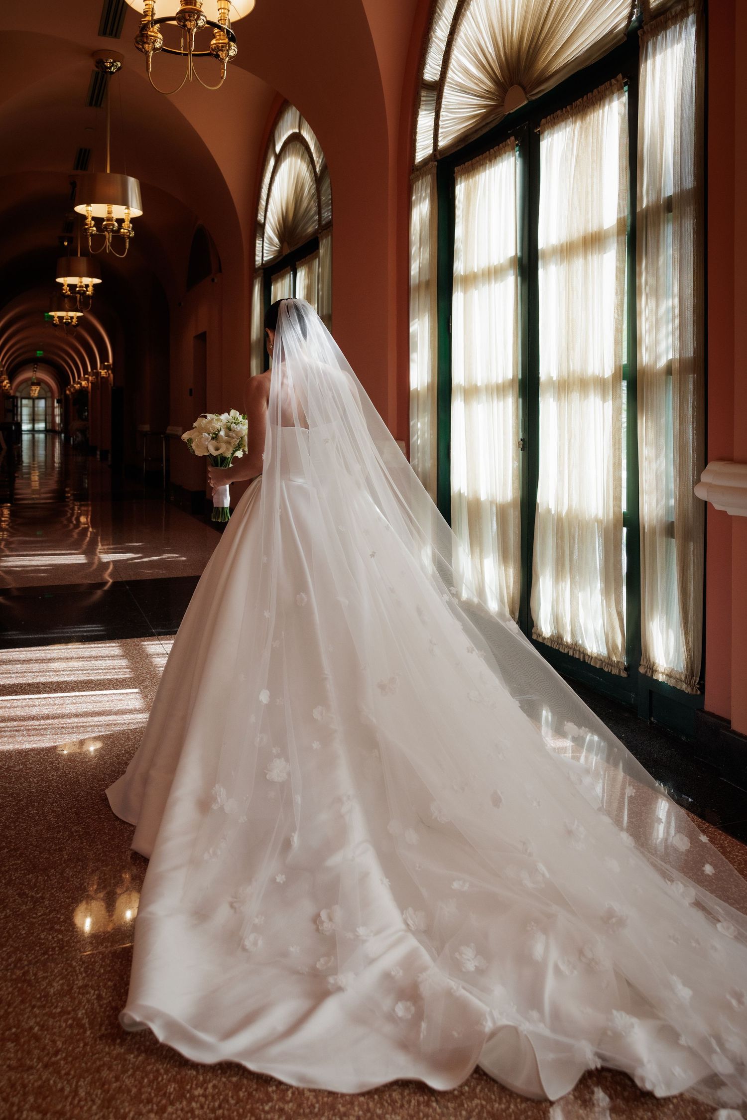 A flowing white wedding gown with a dramatic train photographed in an elegant indoor setting with warm lighting.