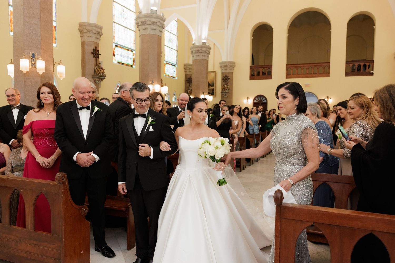 A wedding ceremony procession in a traditional church with white columns and arched ceilings.