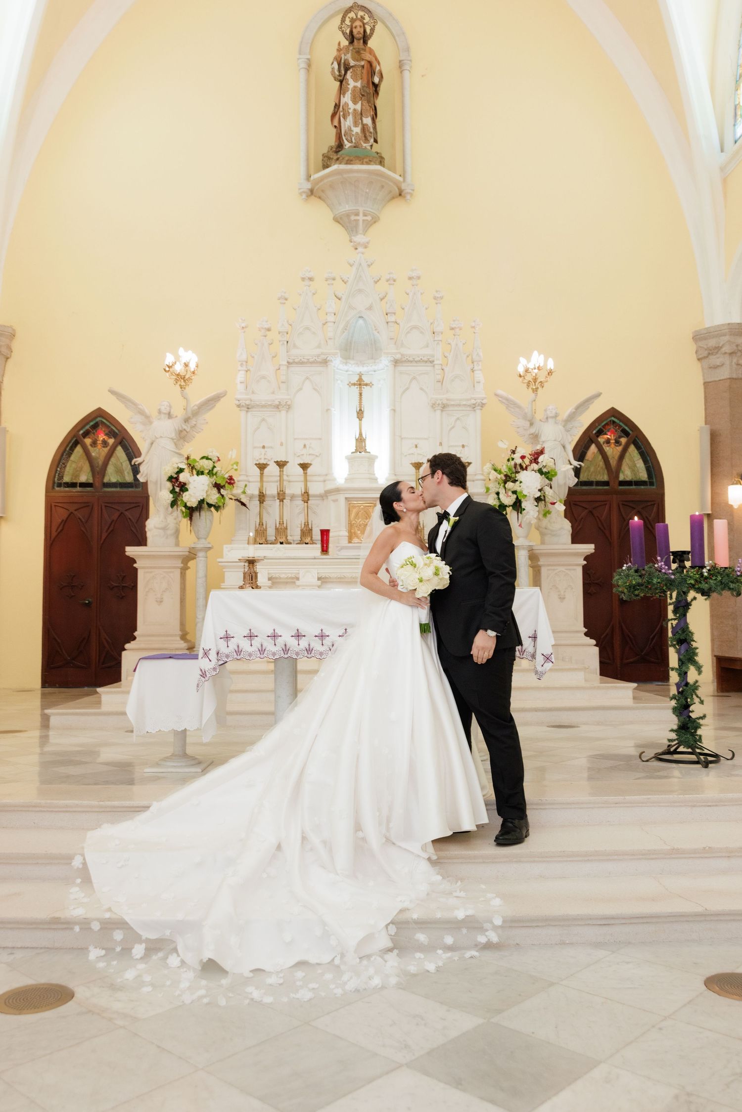 Wedding couple posing in front of an ornate church altar decorated with floral arrangements.