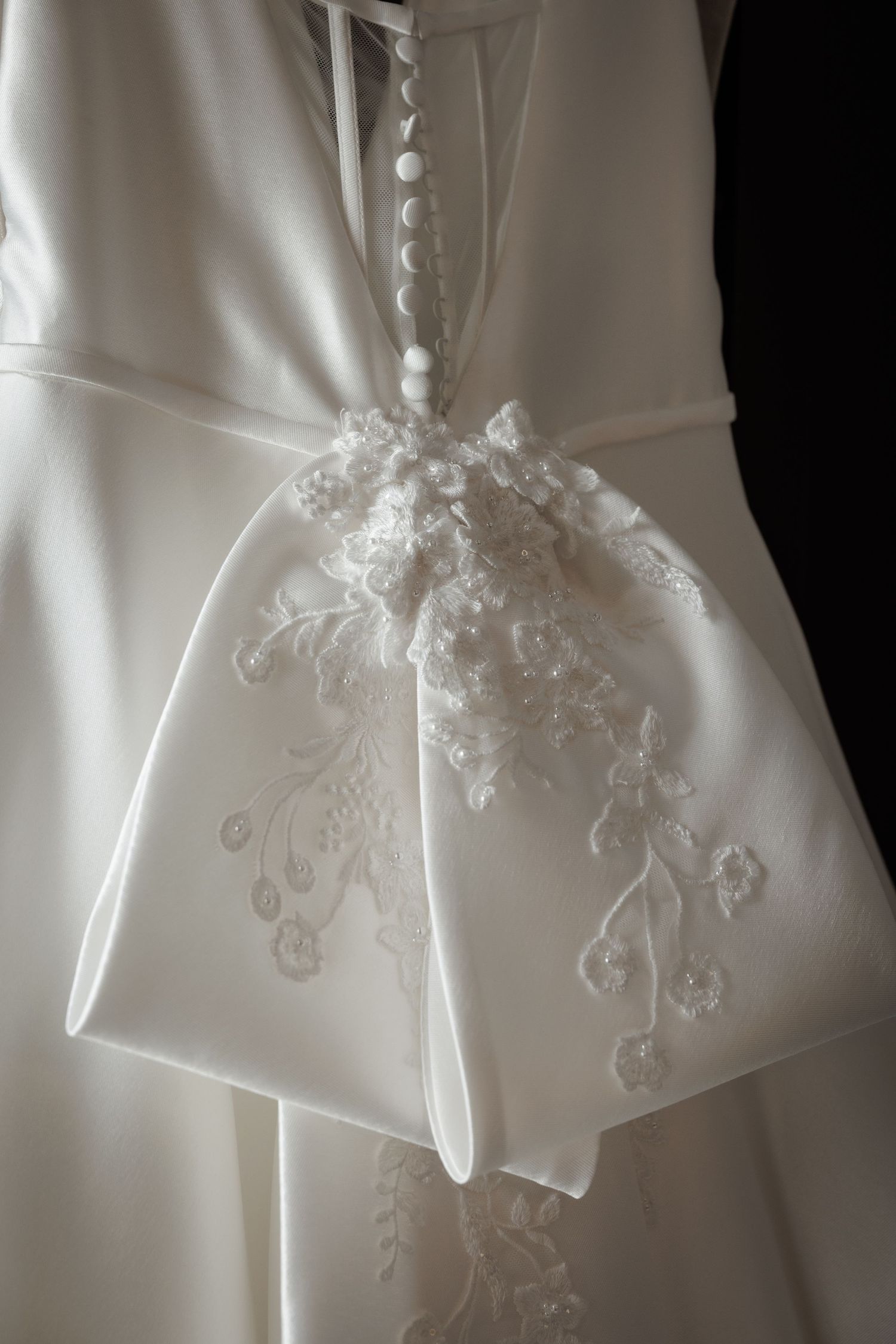 Close-up details of delicate white lace embroidery and beading on a wedding dress bodice.
