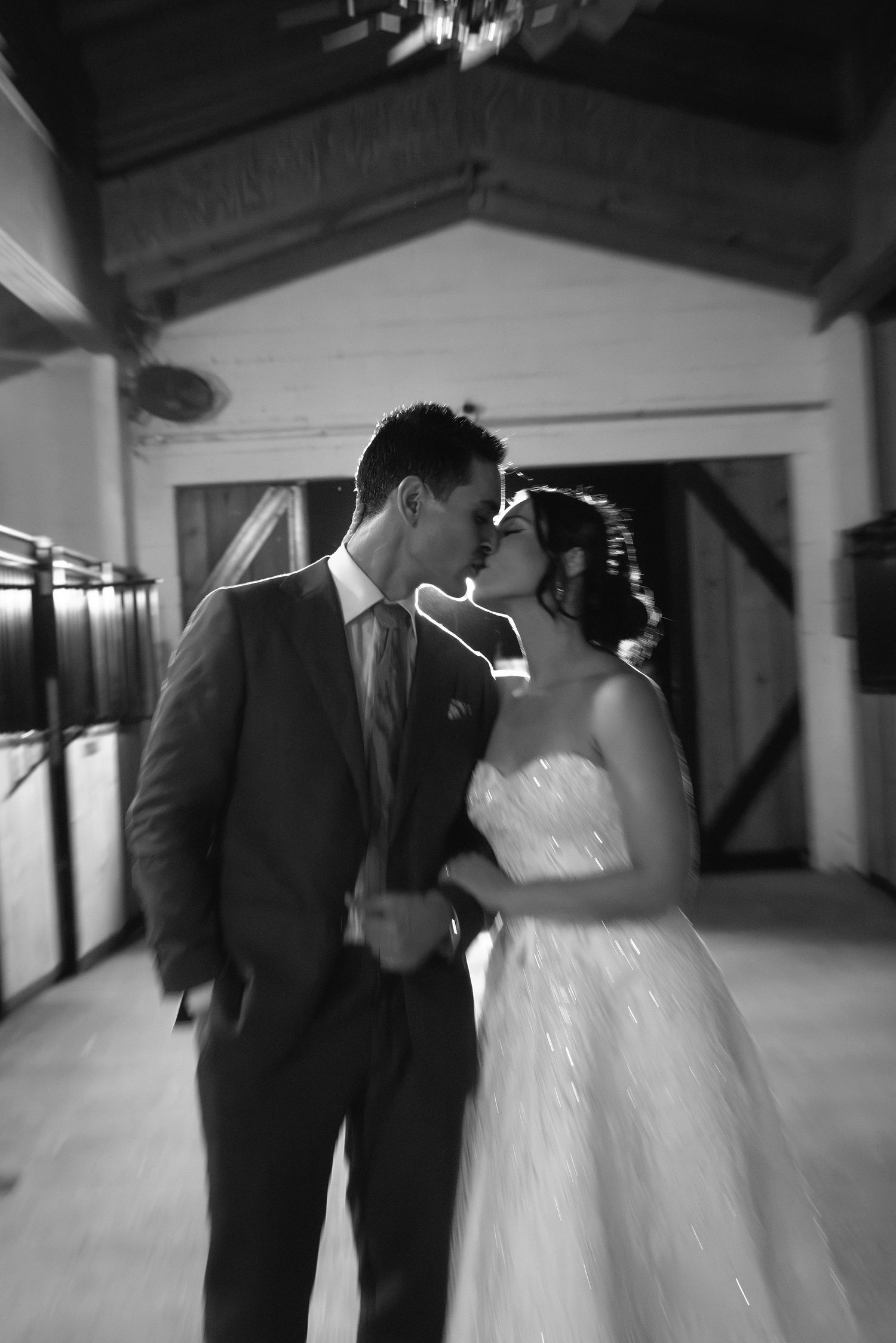 A romantic black and white wedding photo showing a couple sharing a tender kiss in an indoor venue.