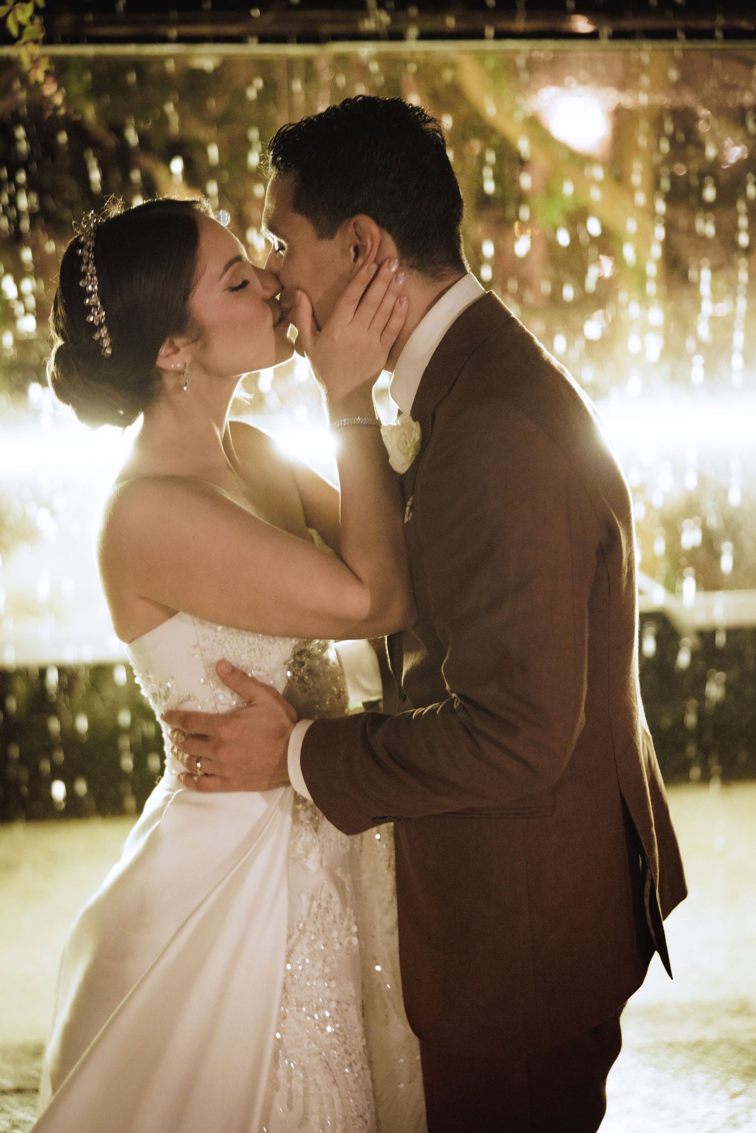 Romantic wedding couple shares a kiss under twinkling lights during their reception celebration.