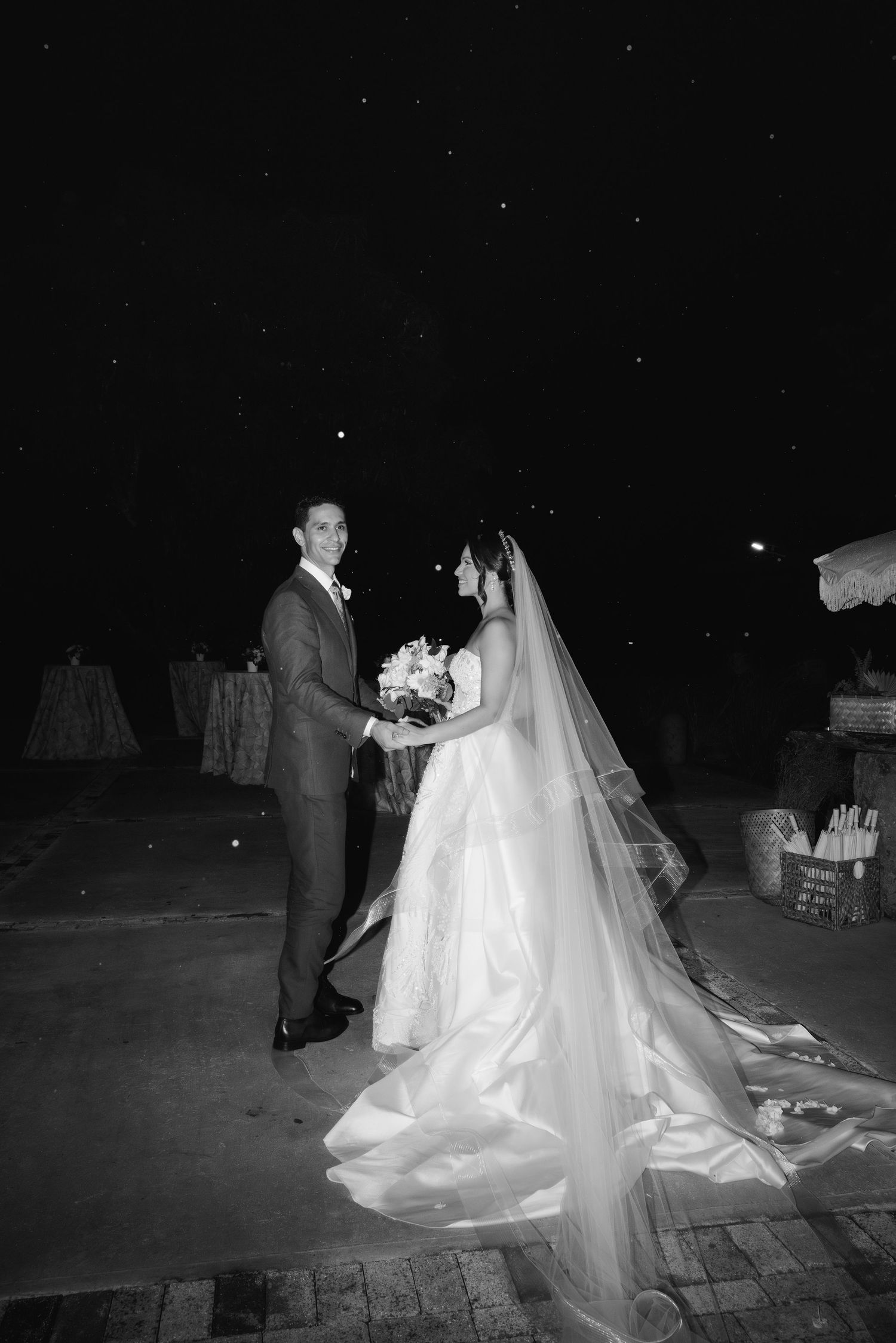 Black and white nighttime wedding portraits on a stone patio with dramatic lighting.