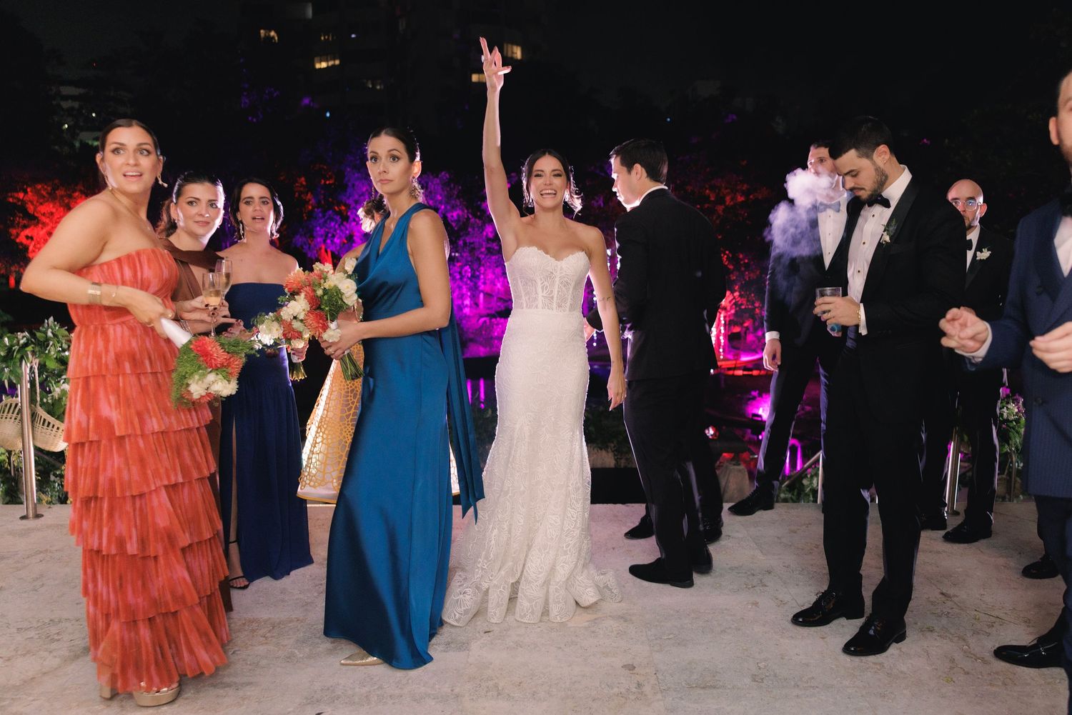 Wedding guests dancing and celebrating at an evening reception with colorful lighting and festive atmosphere.