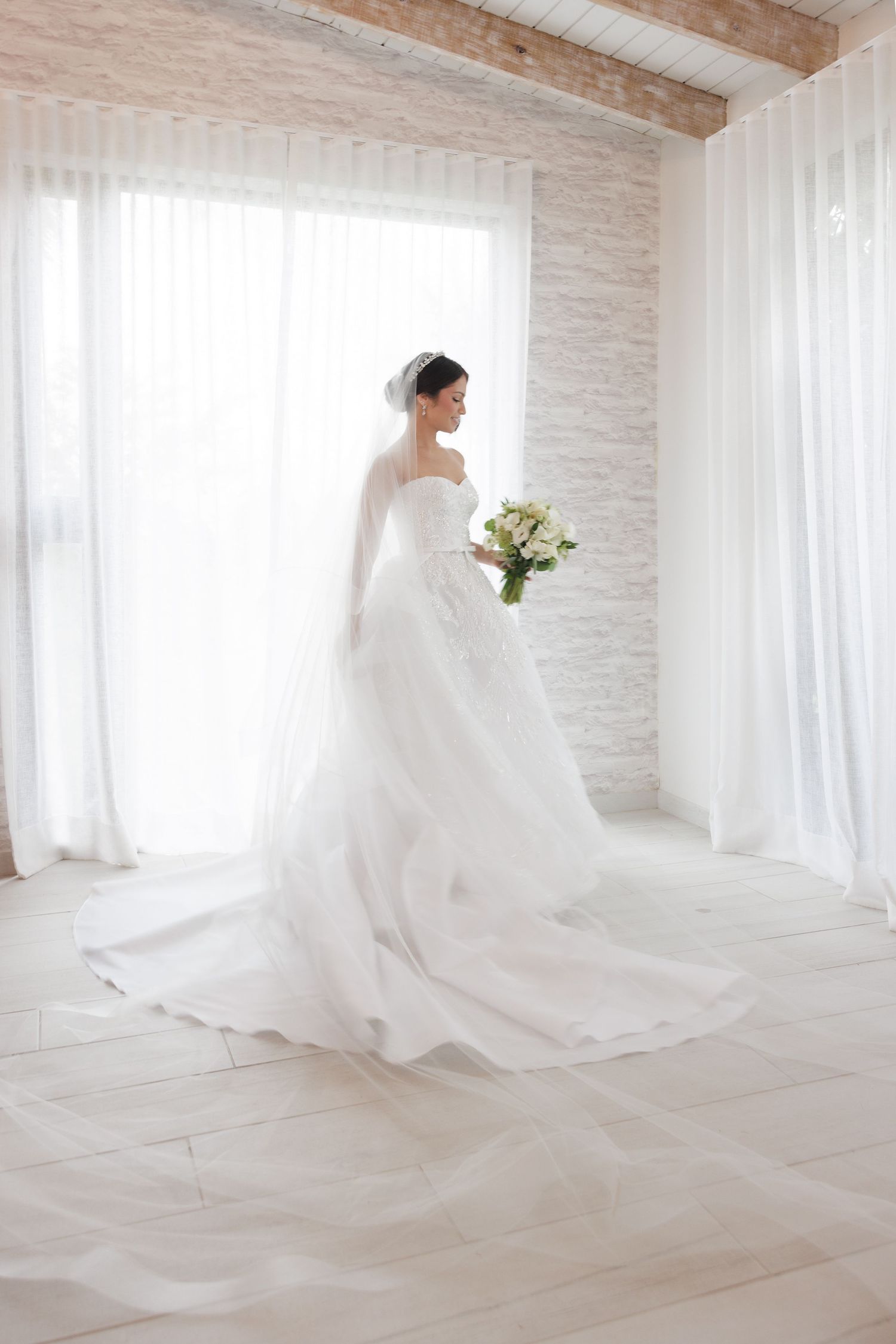 A flowing white wedding dress creates dramatic movement as the bride twirls in a bright, minimalist room.