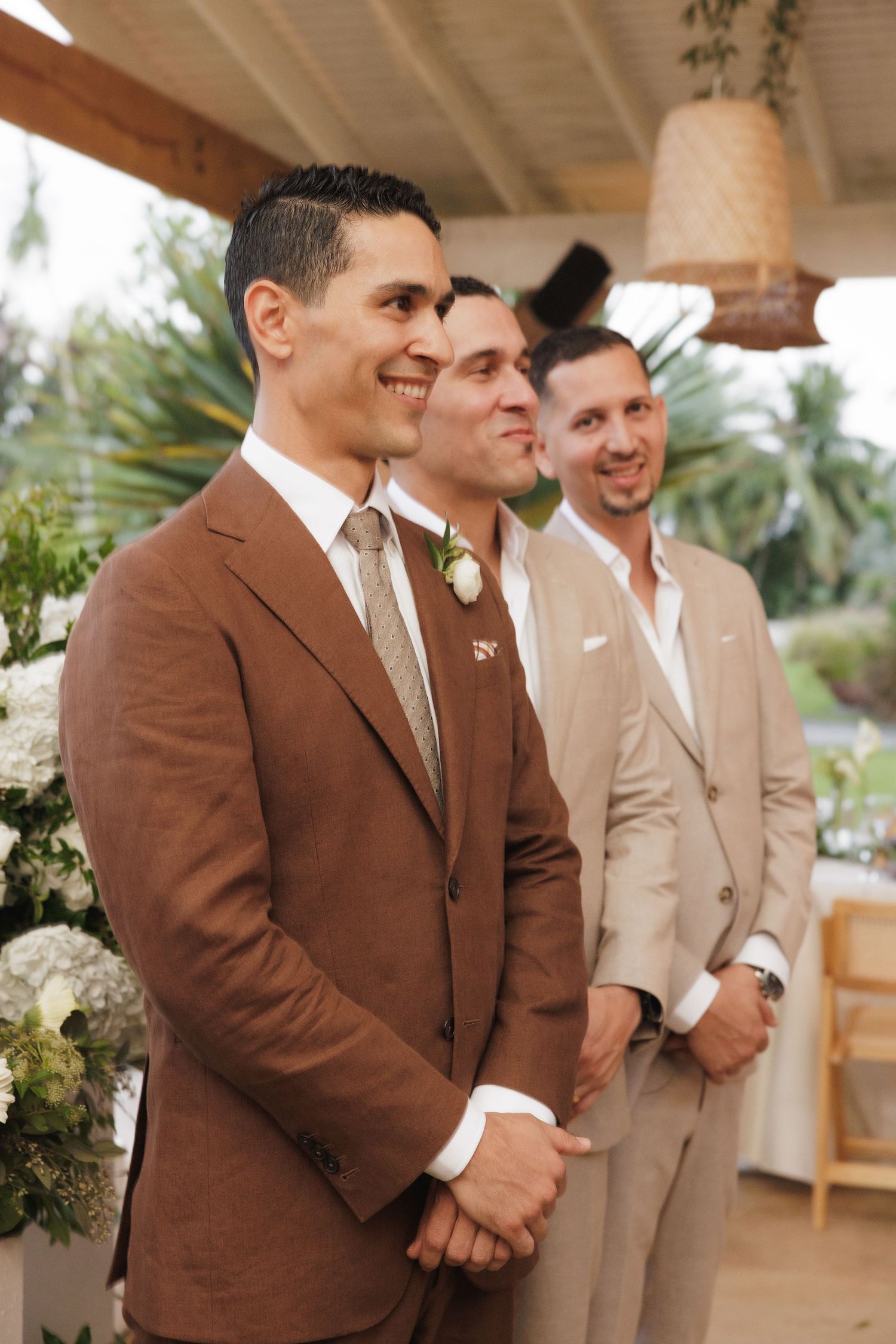 Wedding party members in brown and beige suits stand together during an outdoor ceremony.