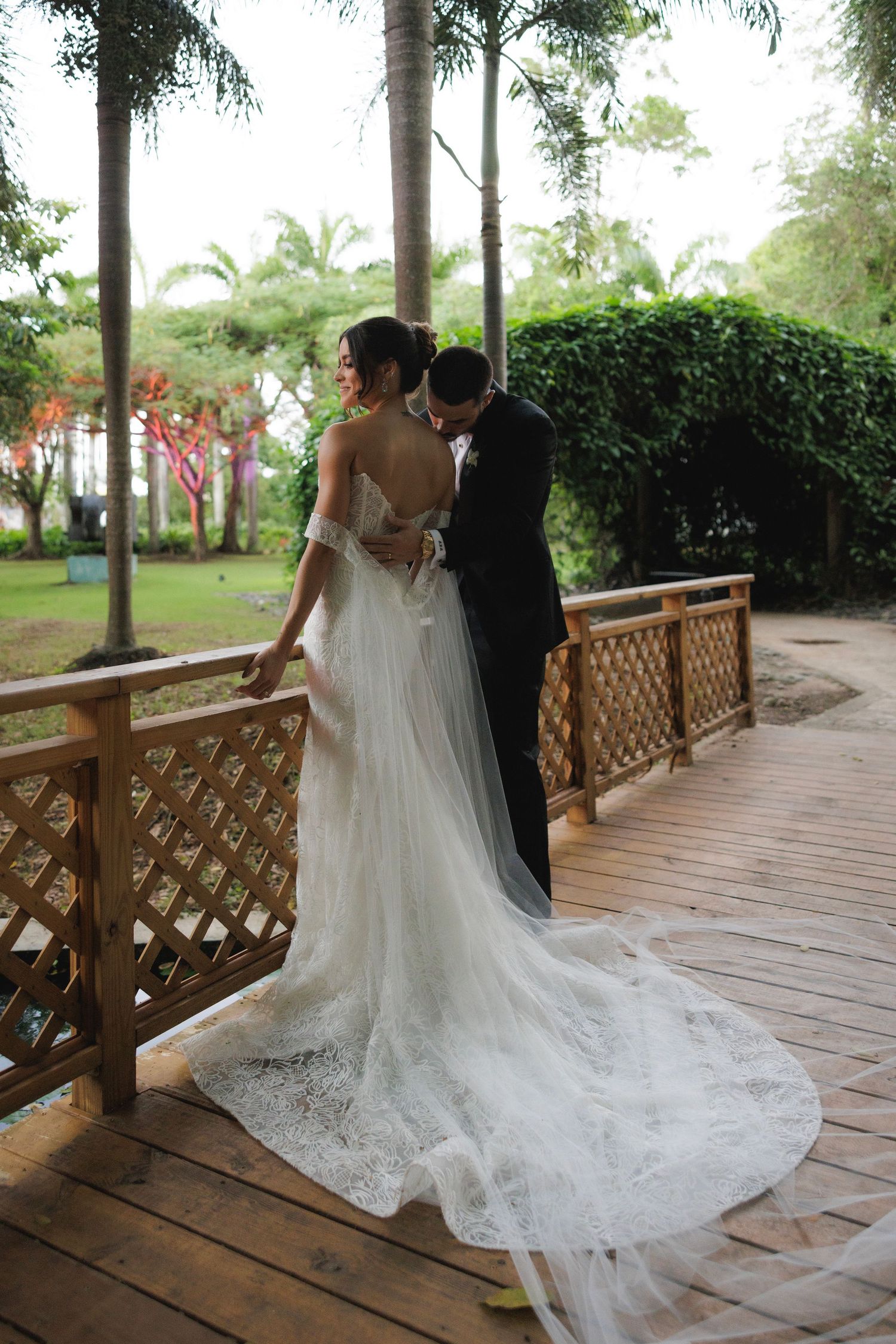 A beautiful wedding scene on a covered outdoor terrace with ornate wooden railings and lush tropical landscaping.
