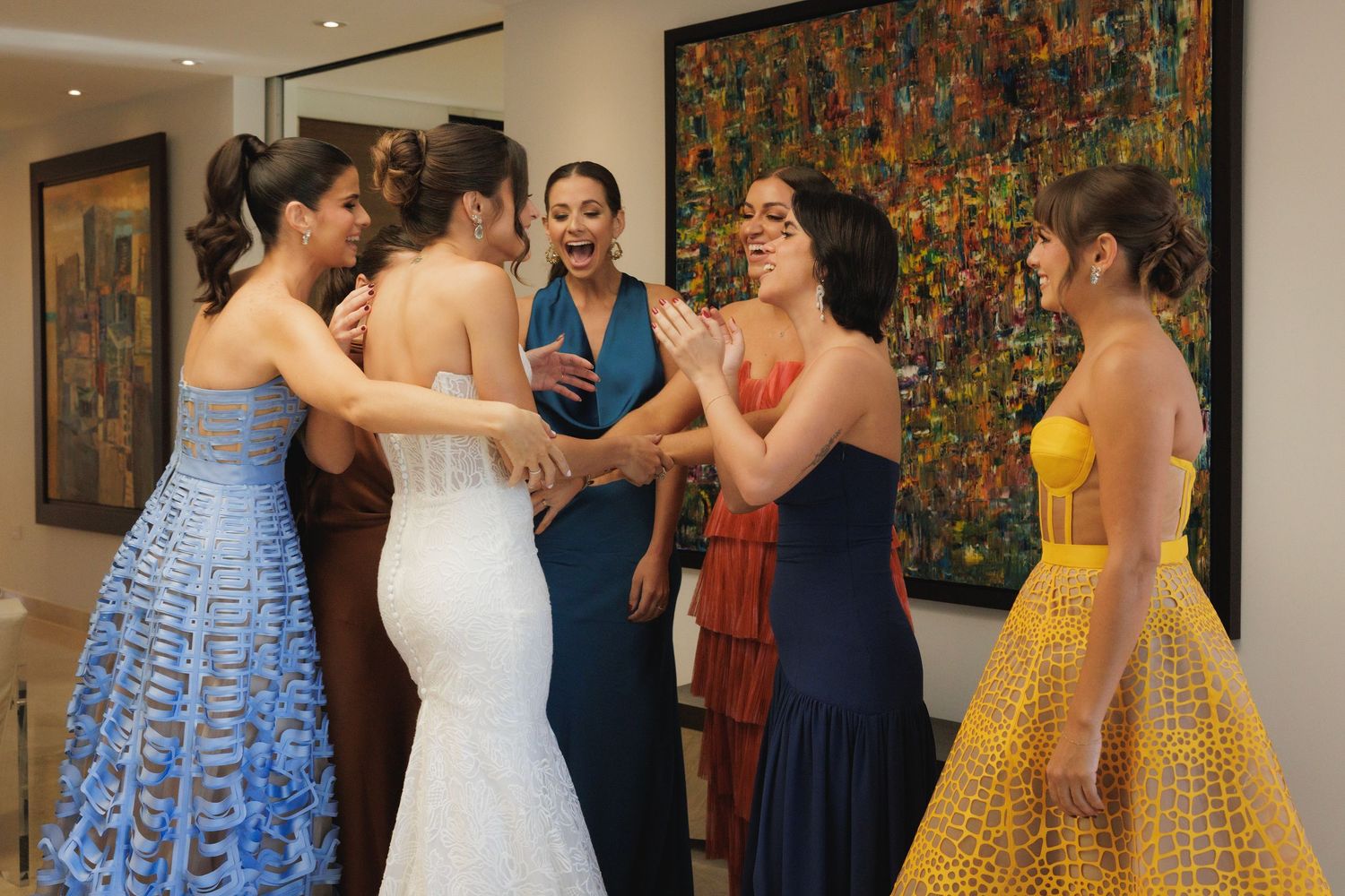 A group in formal attire including colorful gowns in blue, white, navy and yellow gather together at an indoor event.
