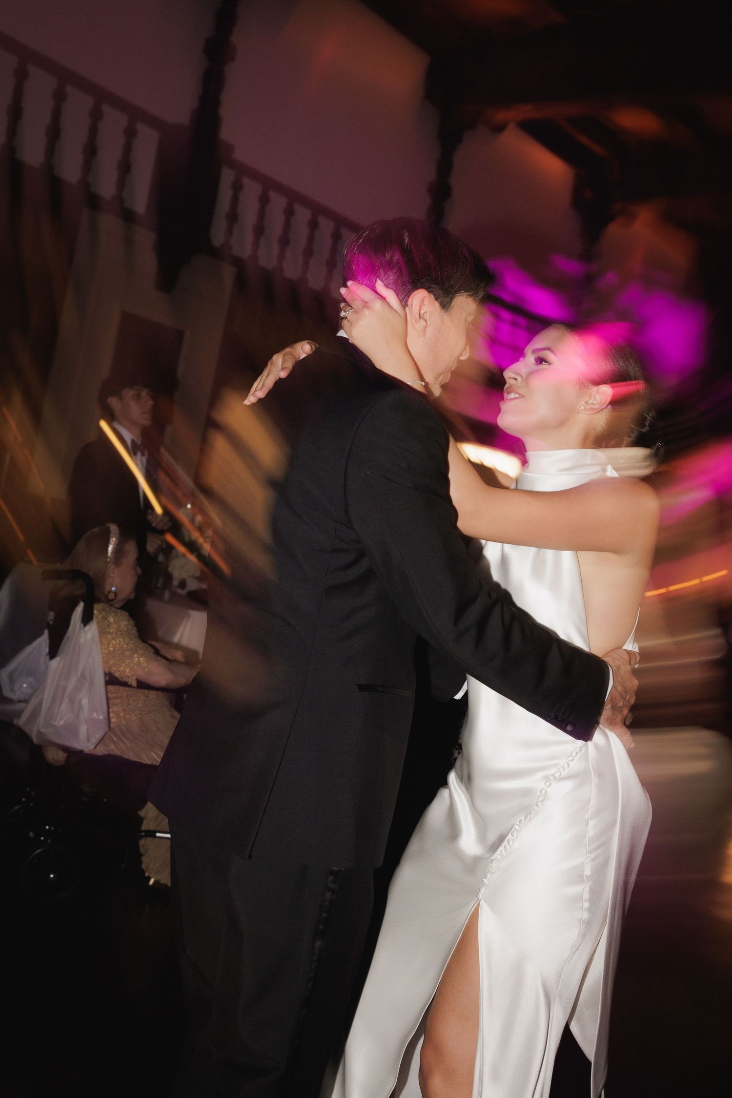 Couple shares romantic first dance at dimly lit wedding reception with purple lighting.