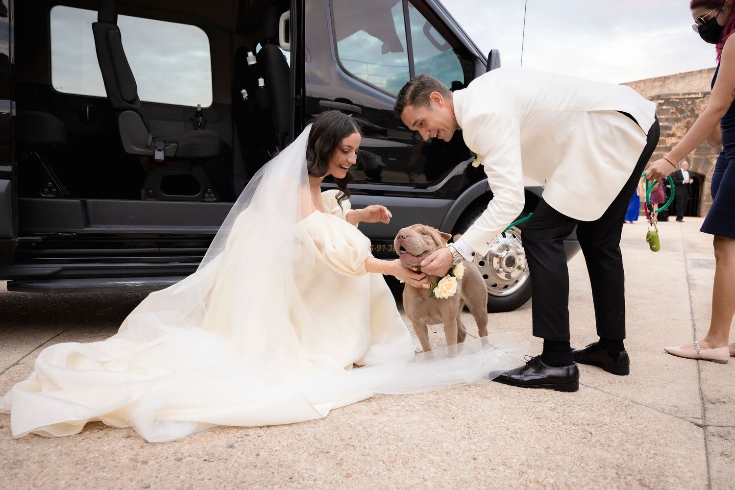 Wedding party helps manage bride's dress train while entering vehicle.