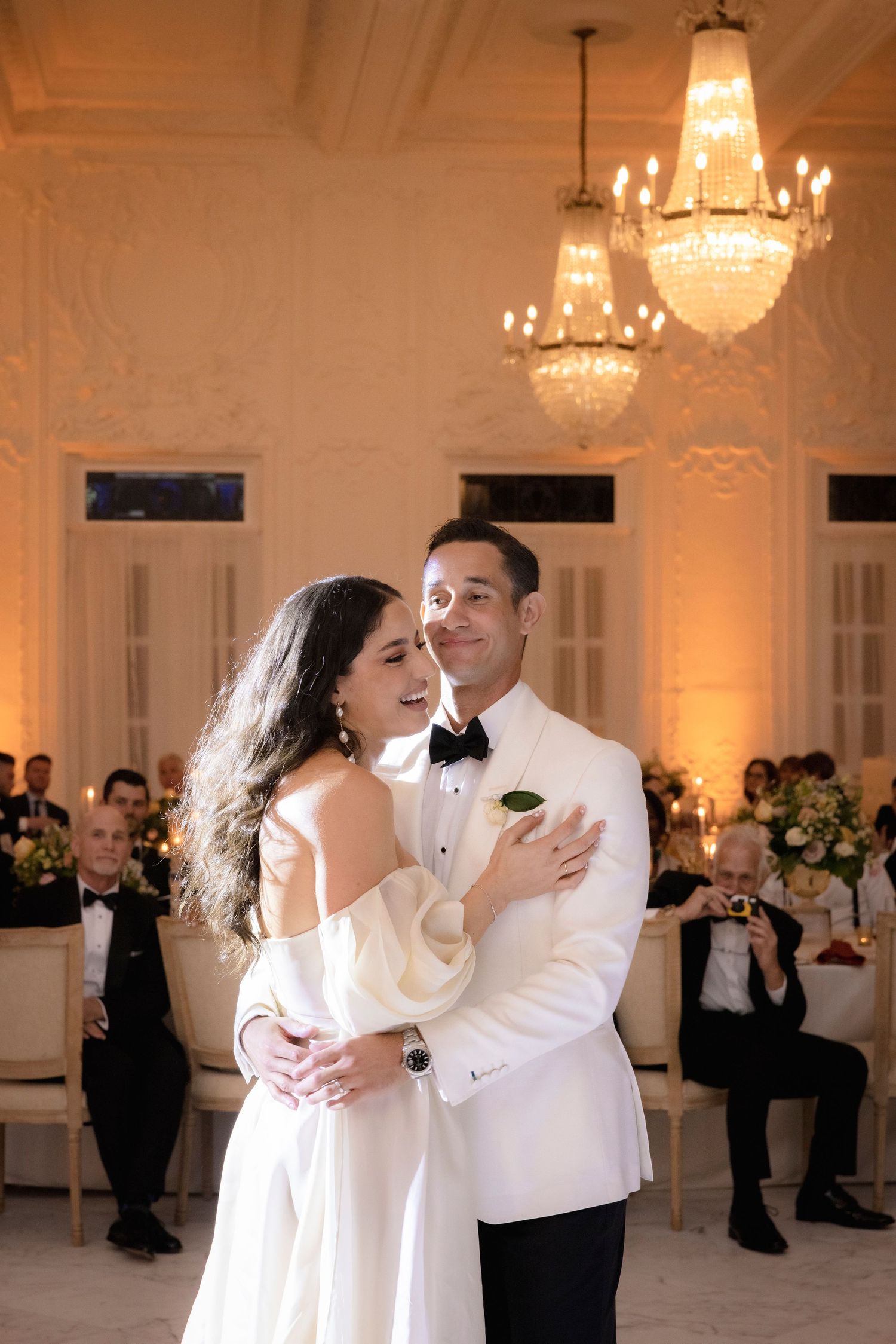 Luxurious ballroom with ornate chandeliers and white decor set for an elegant wedding celebration.