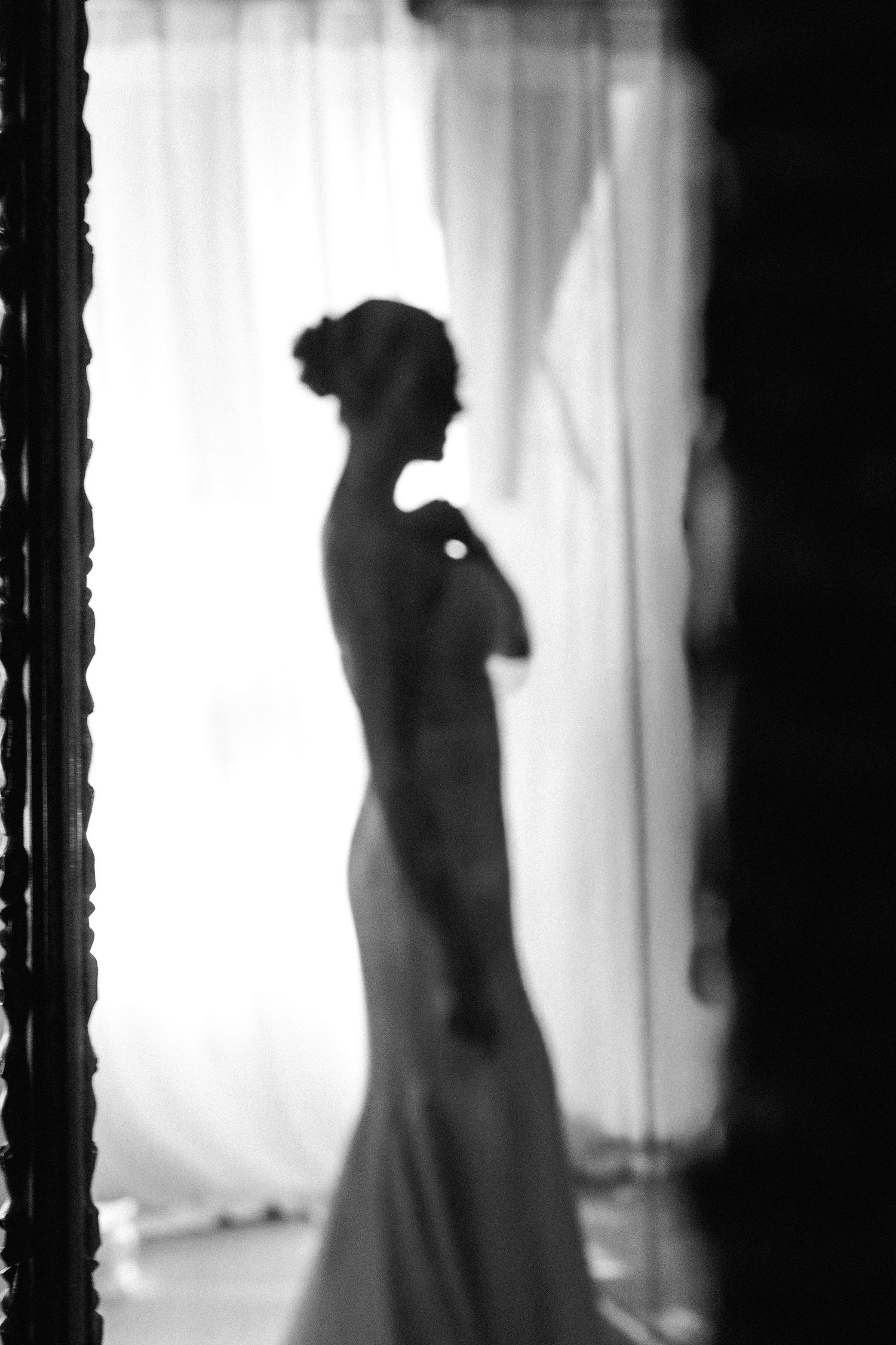 Artistic black and white silhouettes of wedding dress against backlit window.