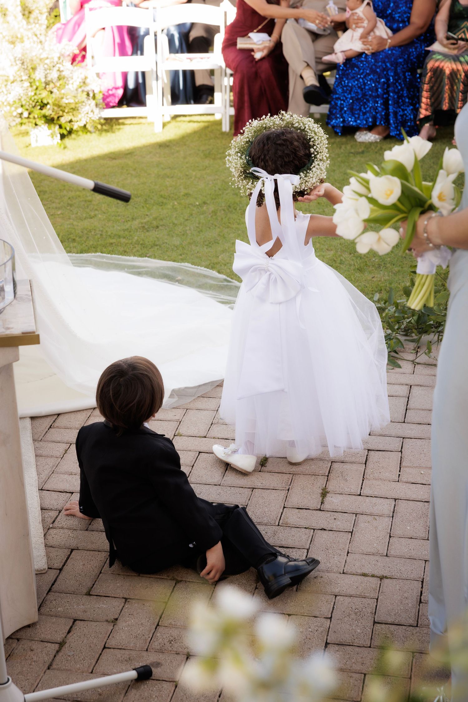 Two young children in wedding attire playing and spinning on a brick patio at an outdoor event.