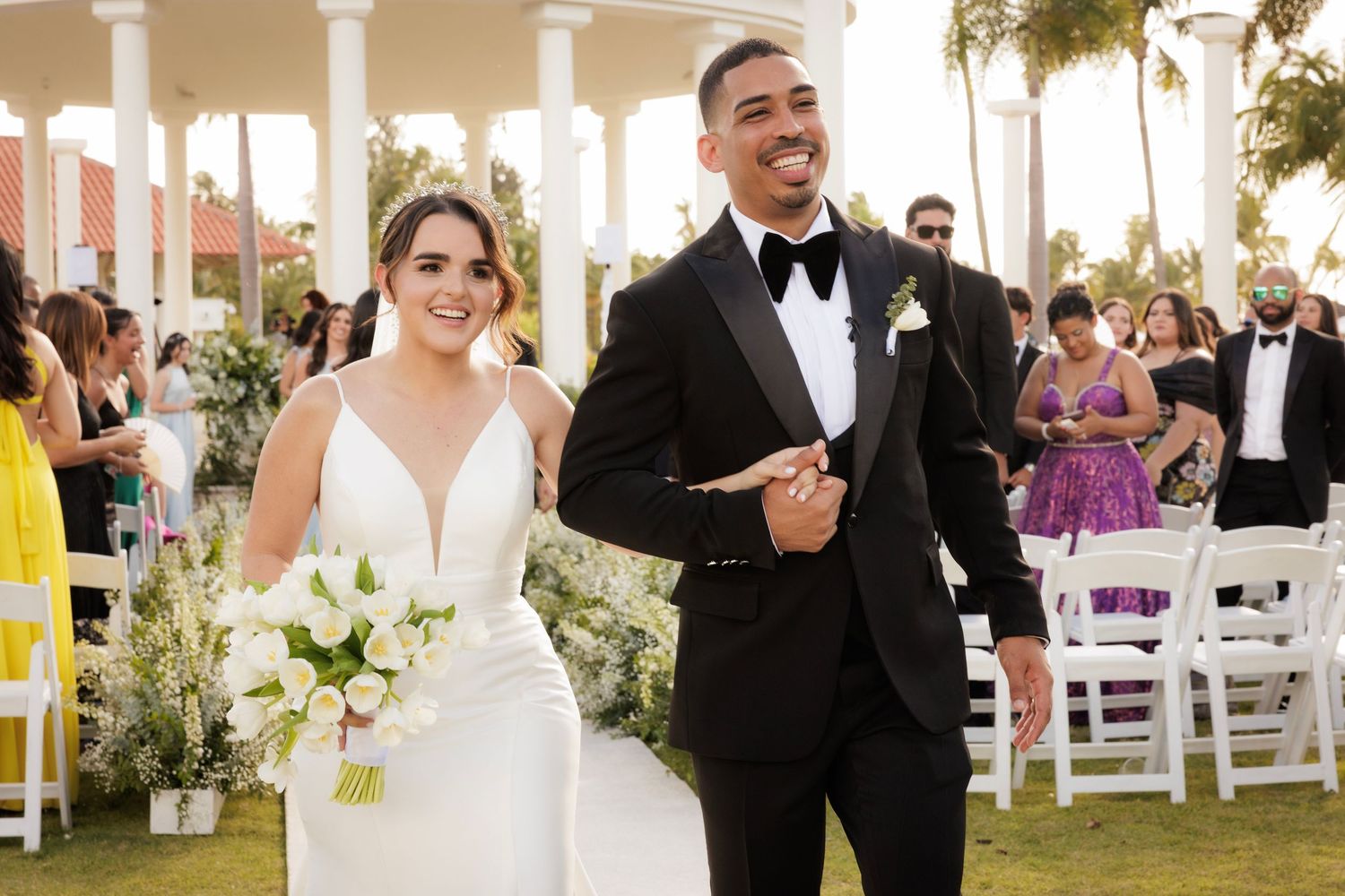 A joyful wedding moment under an elegant colonnade with palm trees and white floral bouquet.