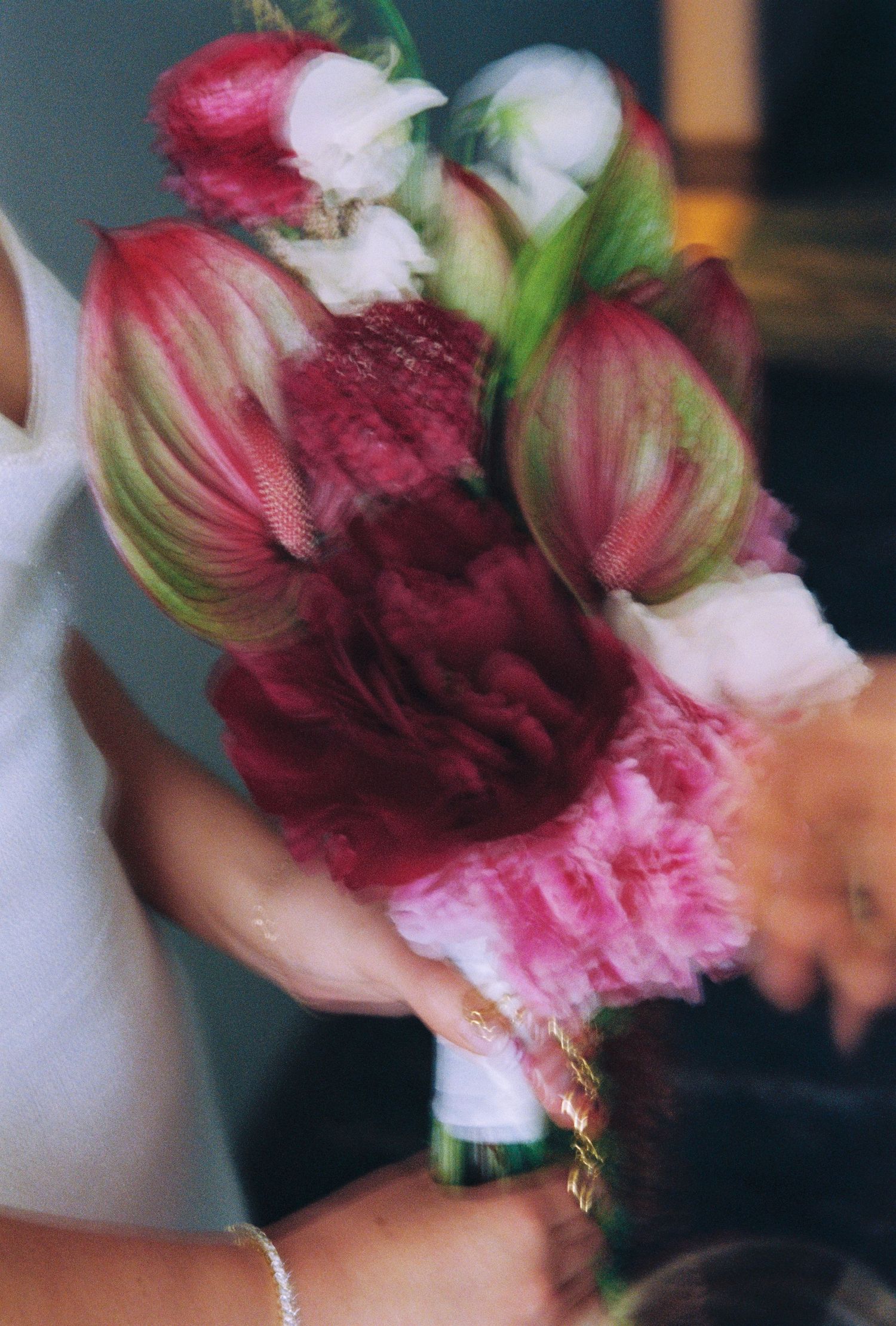 Close-up of a bridal bouquet featuring red anthuriums, pink carnations, and white roses held by the bride.