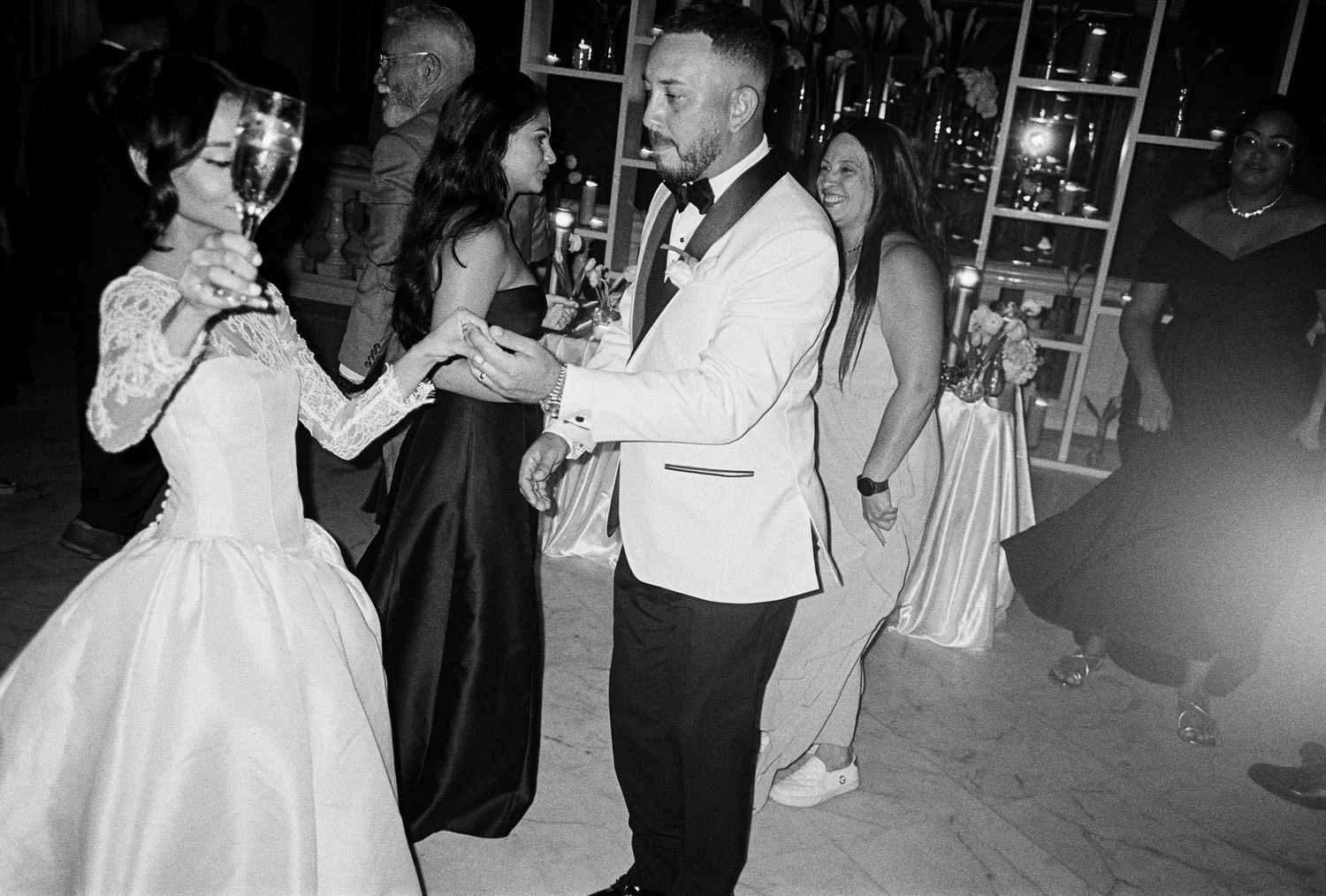 Black and white wedding reception photo of couple dancing with guests celebrating in elegant formal attire.