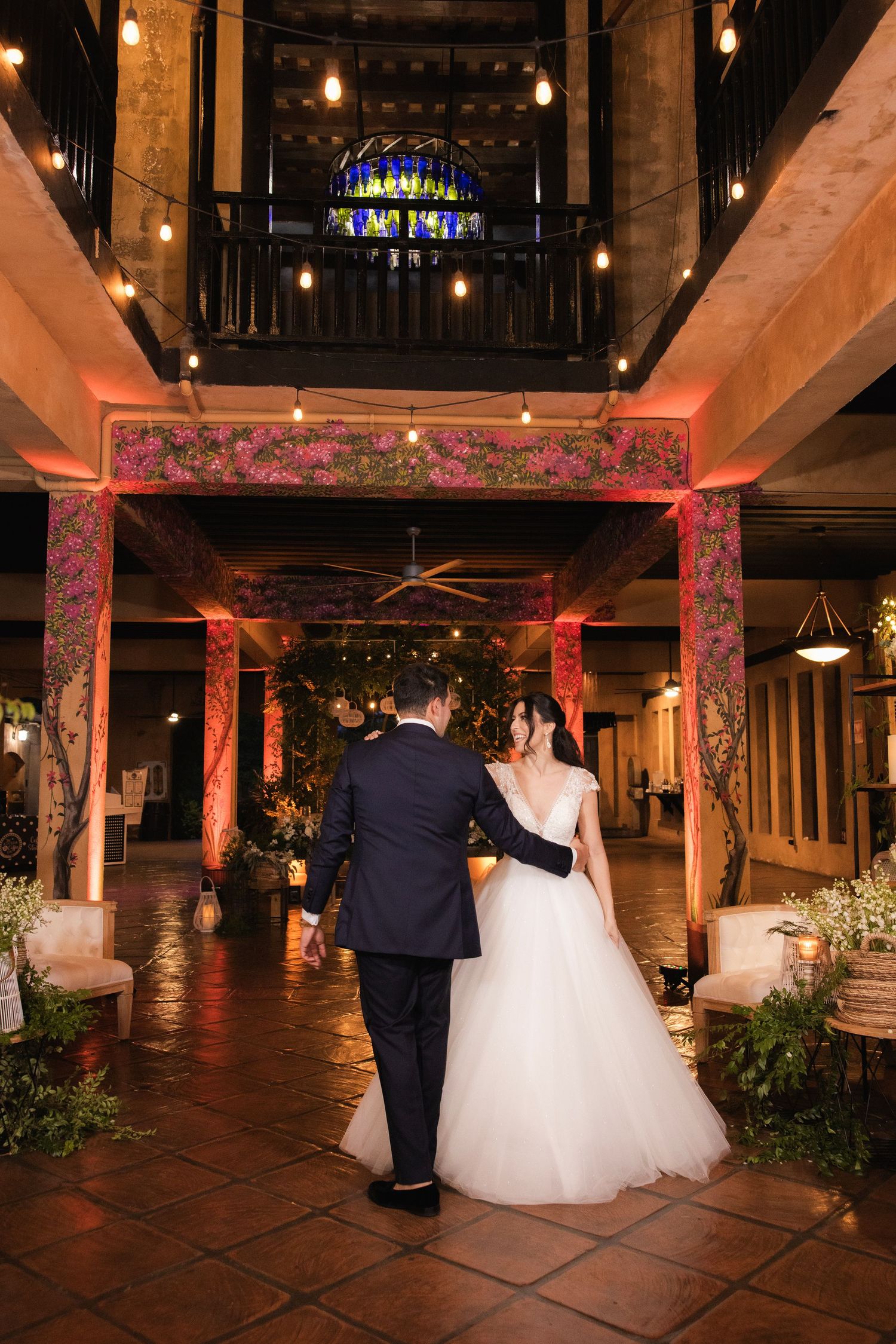 Couple walking through an elegantly lit venue with terracotta tiles and ornate pillars.