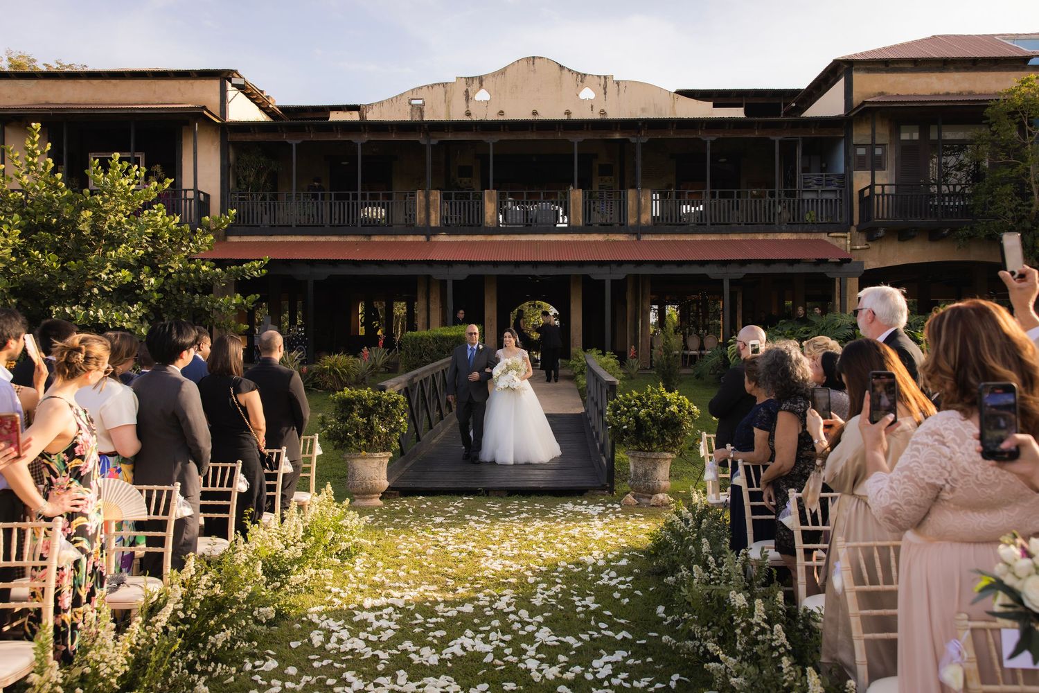 Outdoor wedding venue setup with rustic wooden chairs and natural floral decorations.