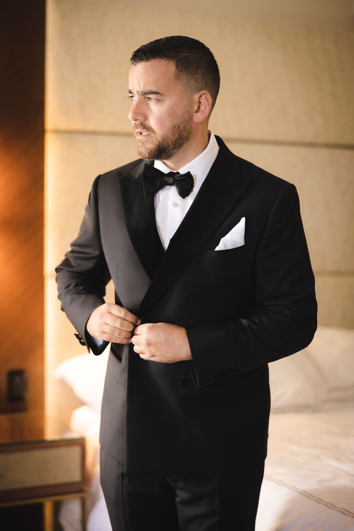 Sharp black tuxedo with bow tie and white pocket square shown against warm interior lighting.