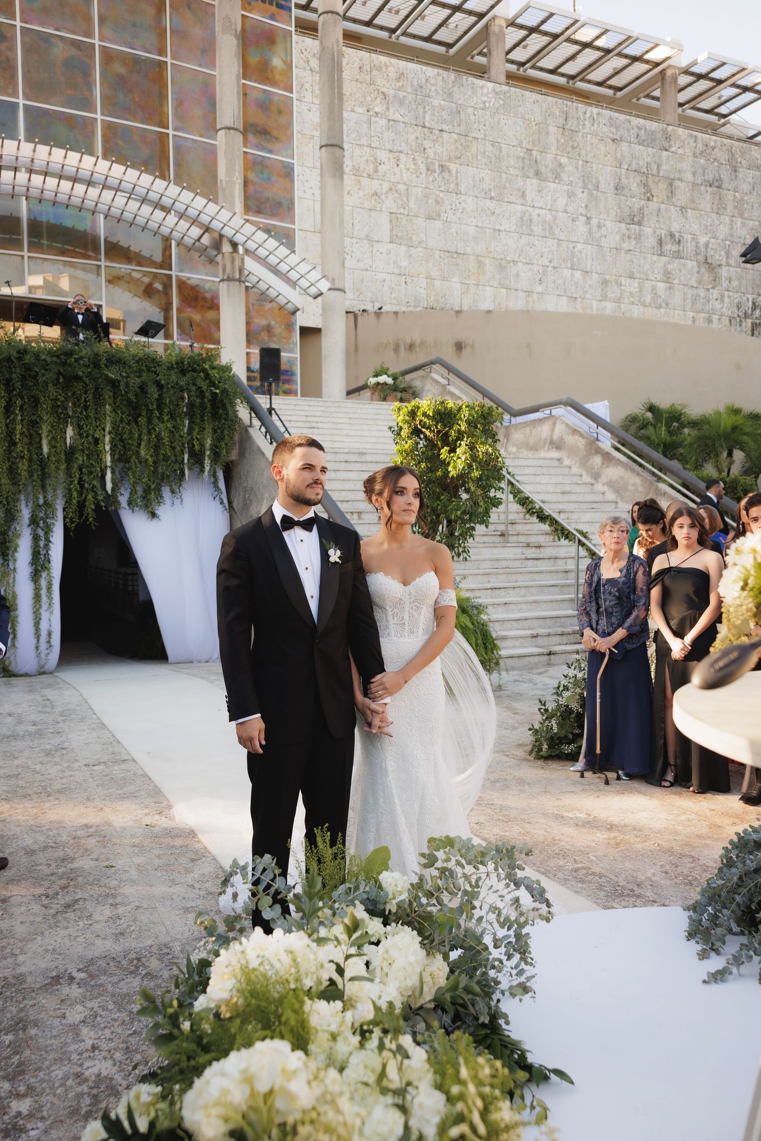 Wedding ceremony space with white draping and greenery against stone architecture.