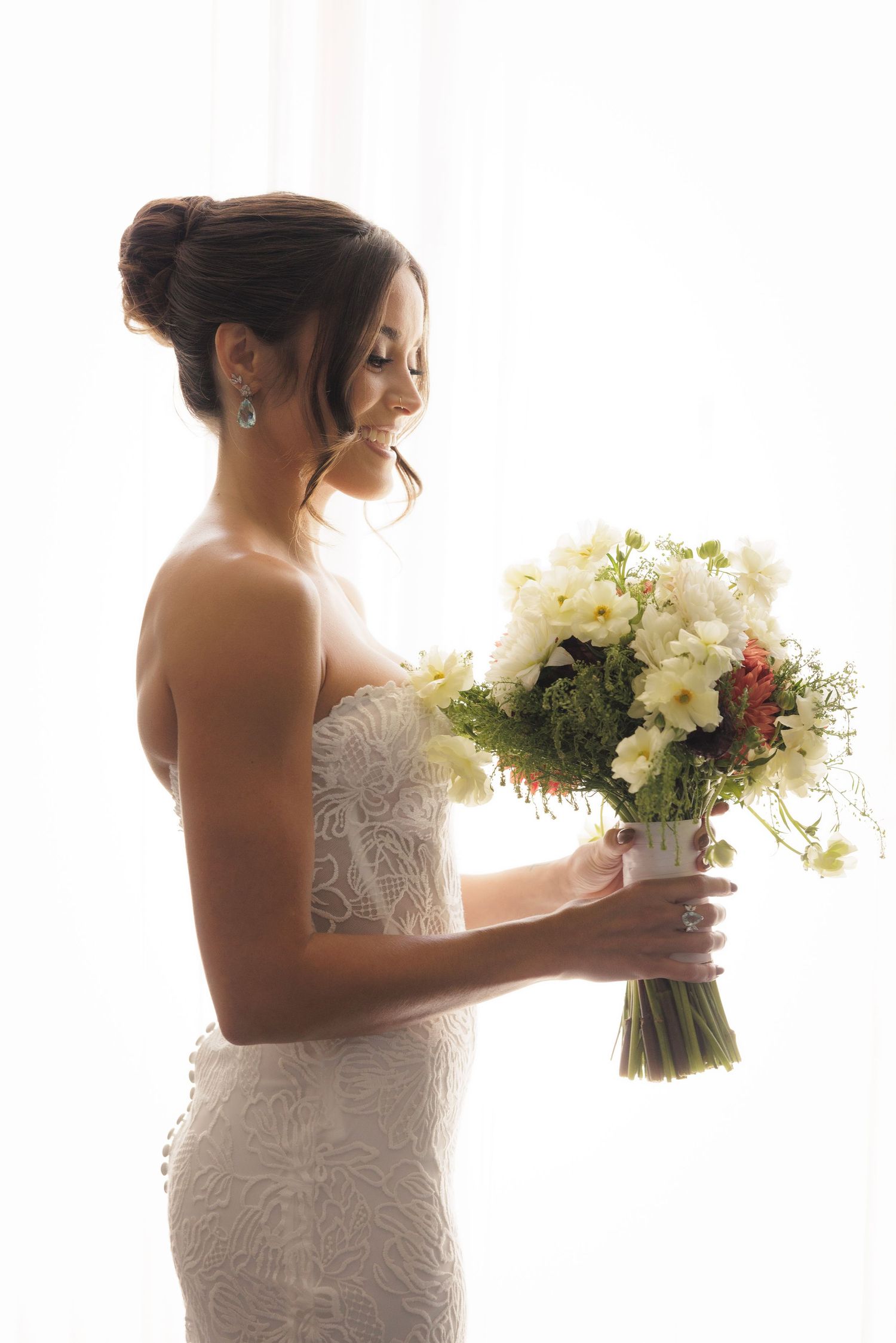 Bride in white lace dress holding beautiful bouquet of white and red flowers in natural light.