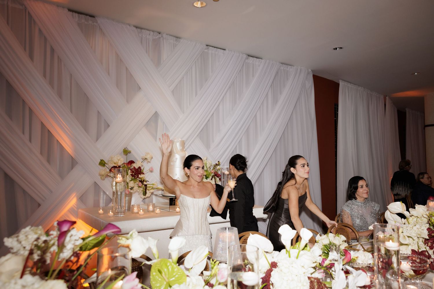 Wedding reception celebration with guests dancing and dining under elegant white draped decor and floral arrangements.