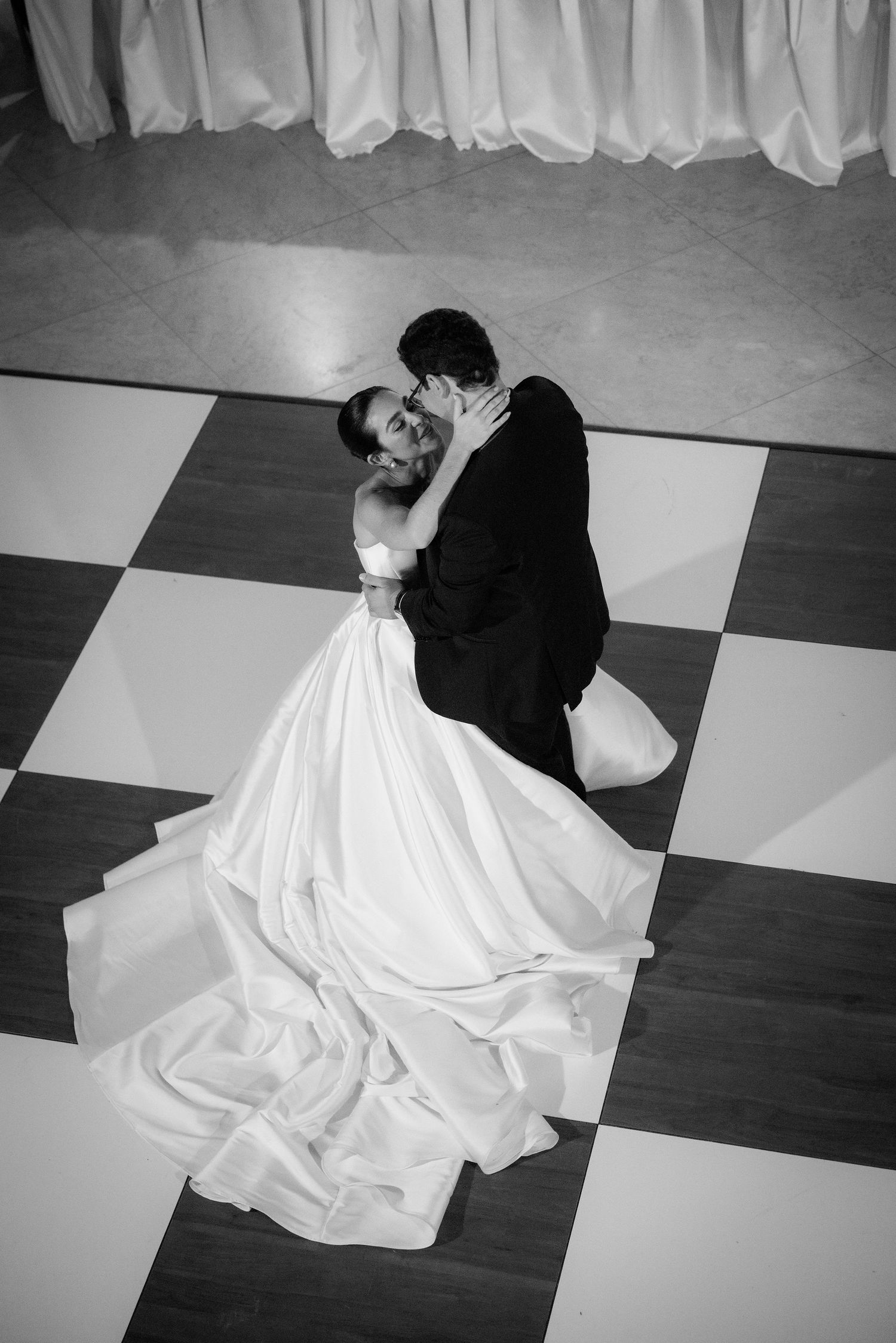 Black and white sequence showing a couple dancing with the bride's white dress flowing across a checkered floor.