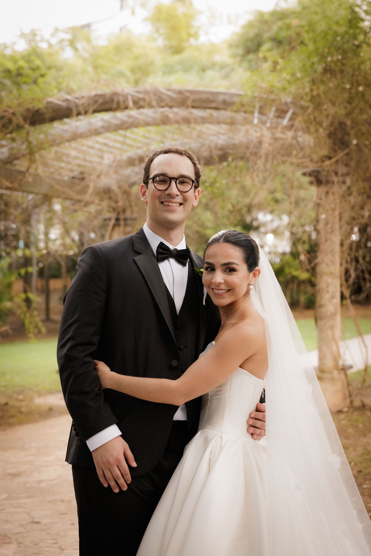 A joyful wedding couple shares a moment on a tree-lined path during their outdoor photo session.
