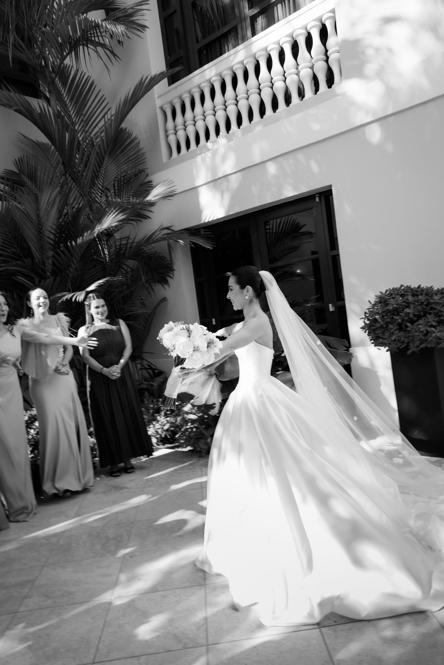 Black and white sequence of a bride twirling in her wedding gown on an outdoor terrace with palm trees.