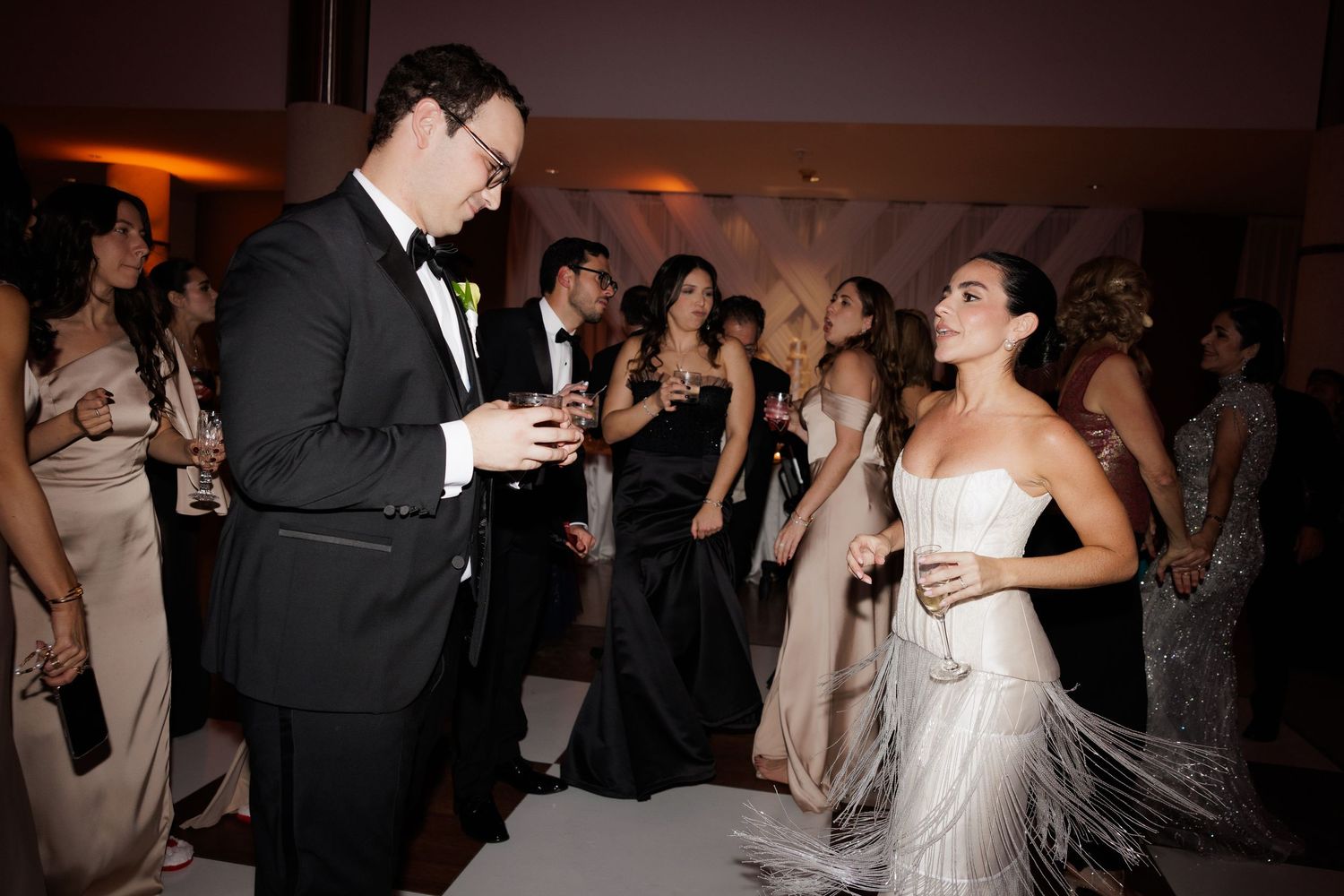 Wedding party enjoying drinks and dancing during an evening reception celebration.