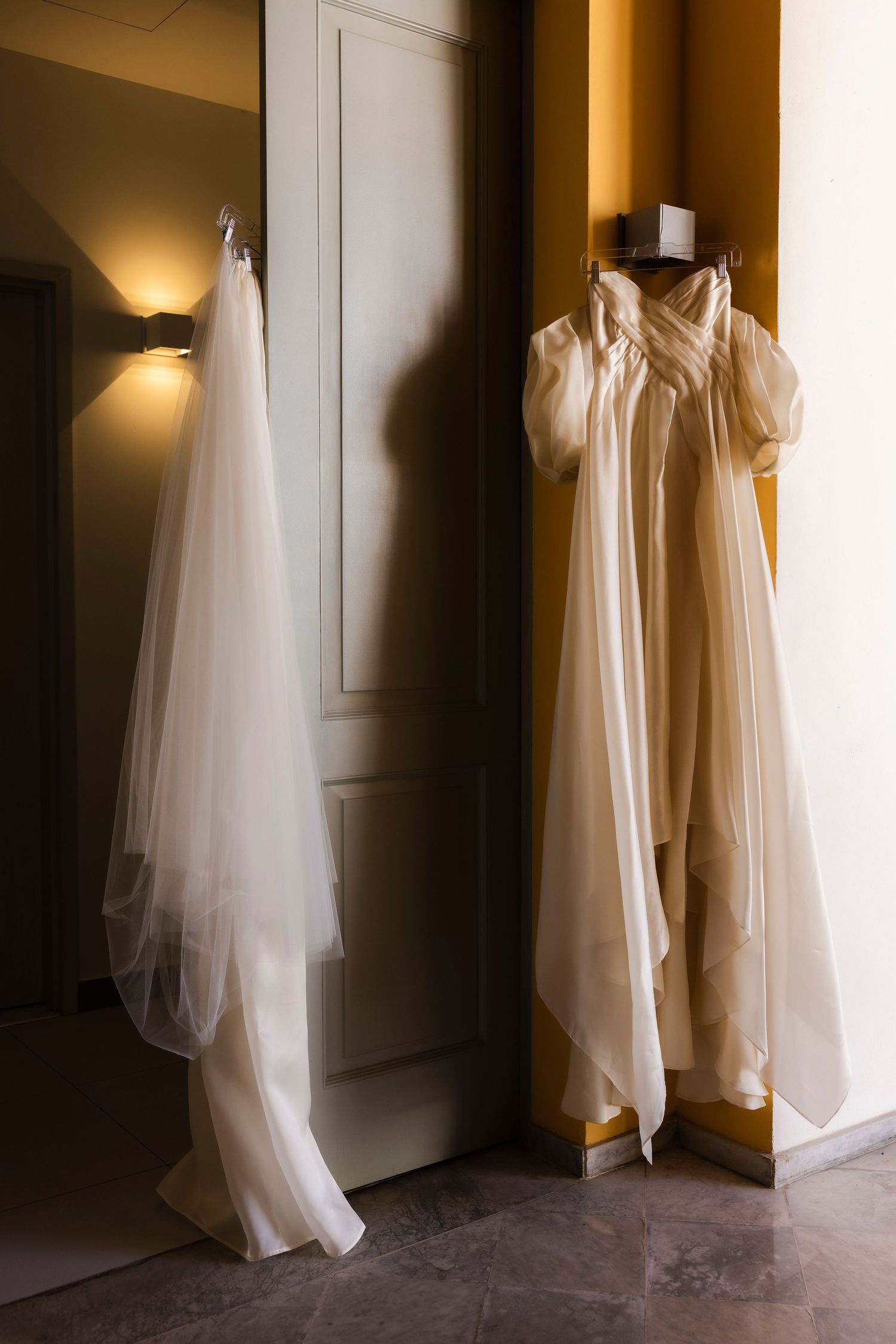 White flowing wedding dress materials draped elegantly against a moody dark wall in dramatic lighting.