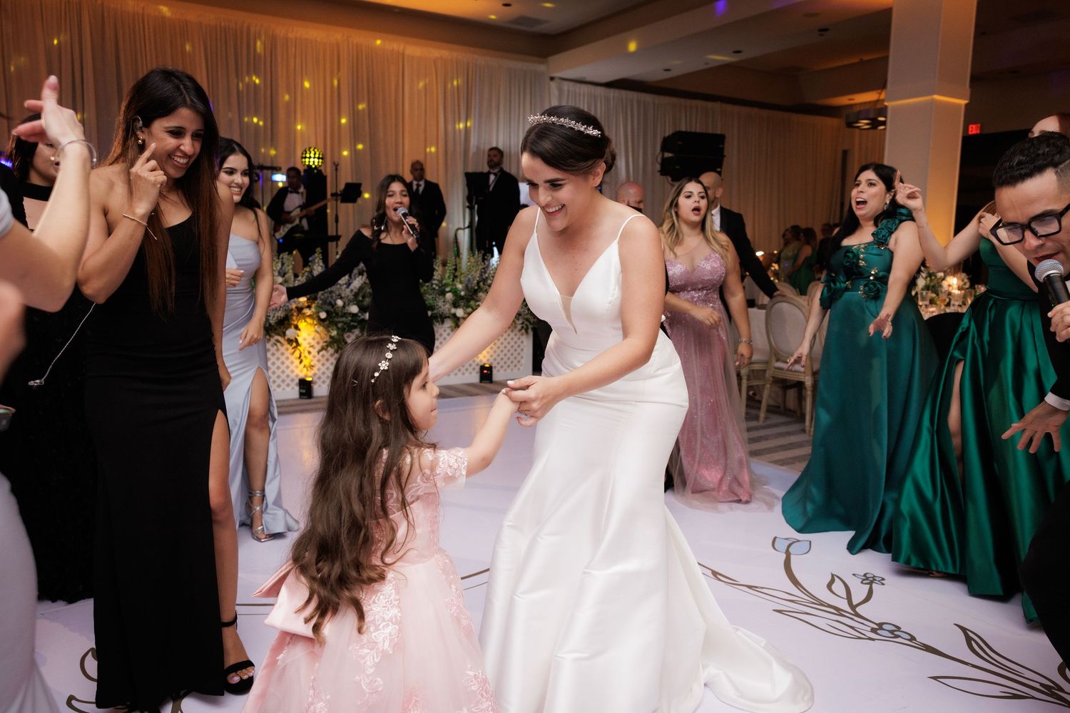 Wedding guests in emerald green and pink dresses dance together on a lively reception dance floor.