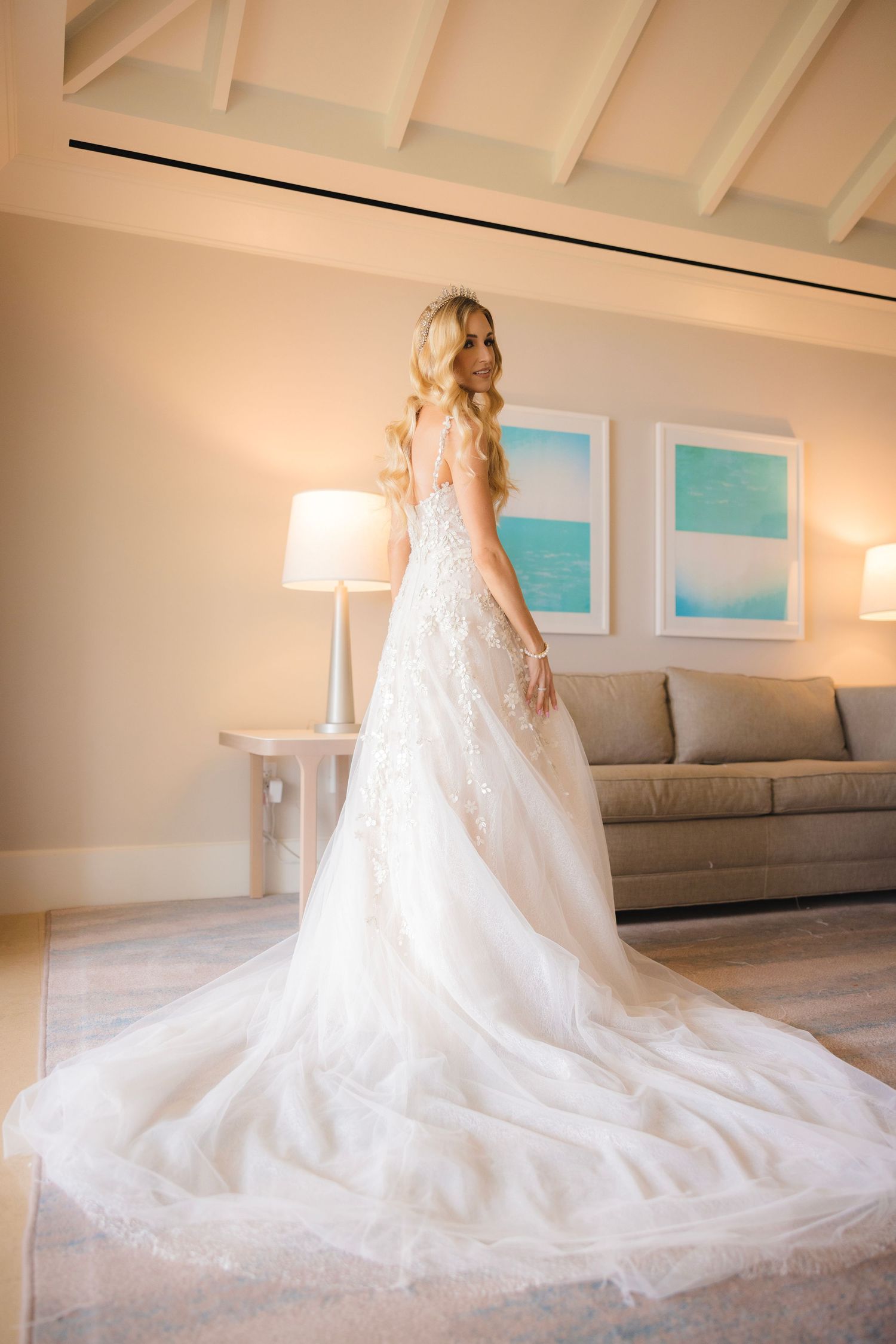 A bride in an elegant white wedding gown with a dramatic long cathedral train on light colored hardwood flooring.