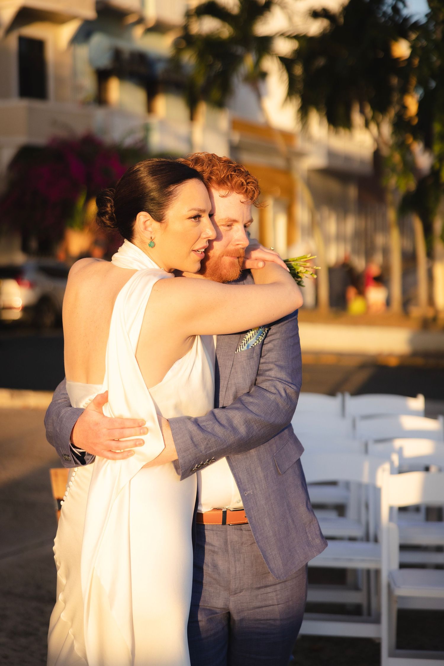 Two people embracing at an outdoor wedding ceremony with white chairs in the background.