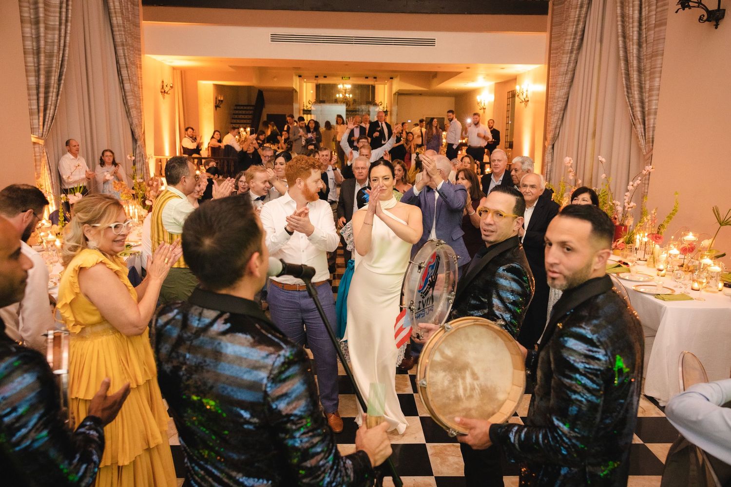 Wedding guests dance and celebrate on a crowded dance floor during an evening reception in an elegant ballroom.