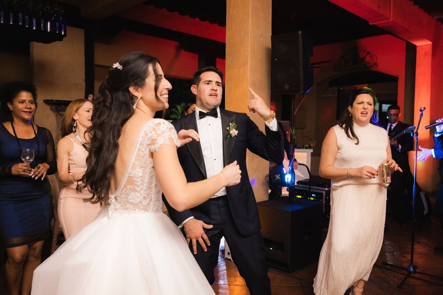 Reception guests dance and mingle on a wedding dance floor illuminated by red ambient lighting.