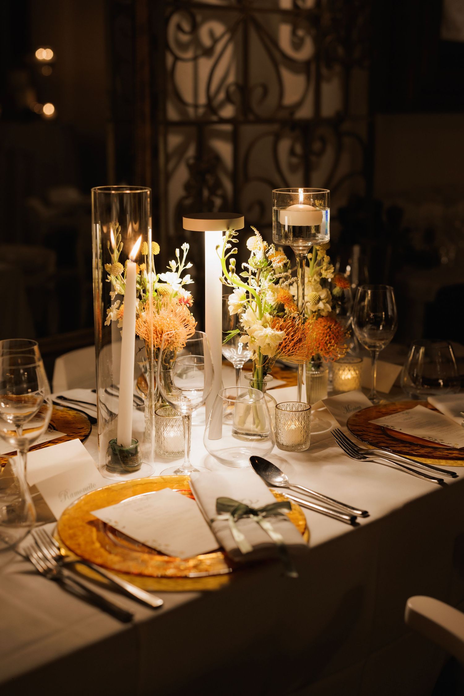 Elegant dinner table settings with white candles, soft lighting, and floral centerpieces in a dimly lit restaurant.