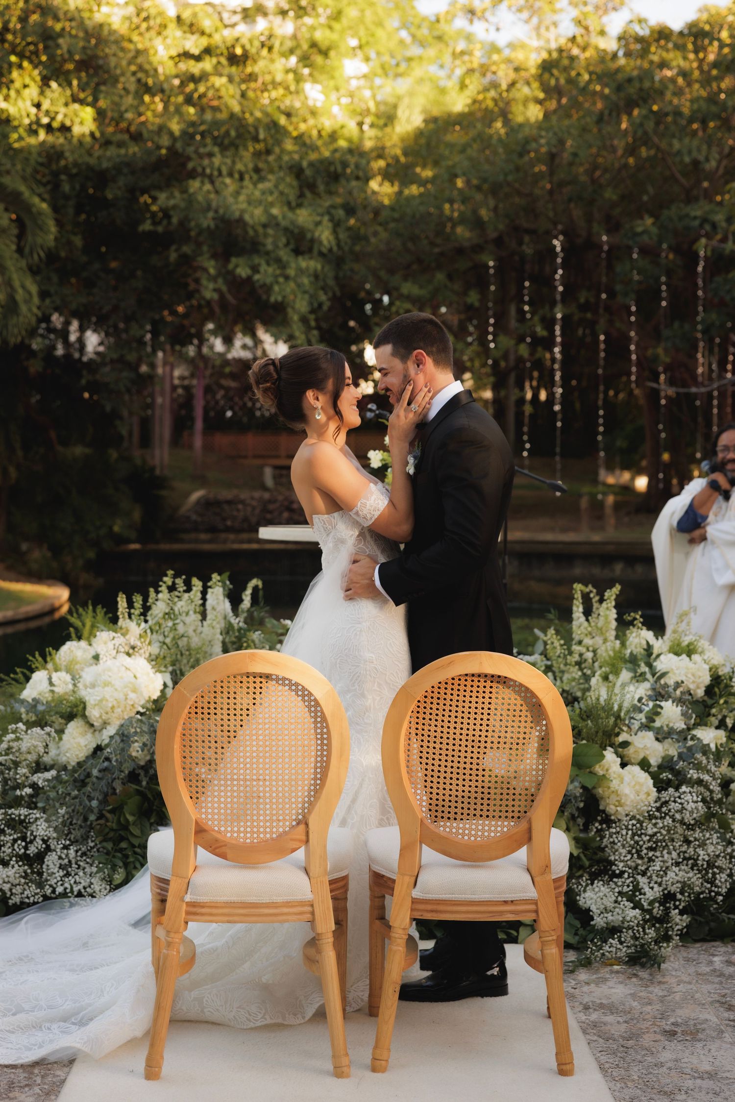 Wedding ceremony setup with two wooden chairs outdoors surrounded by white floral arrangements and string lights.