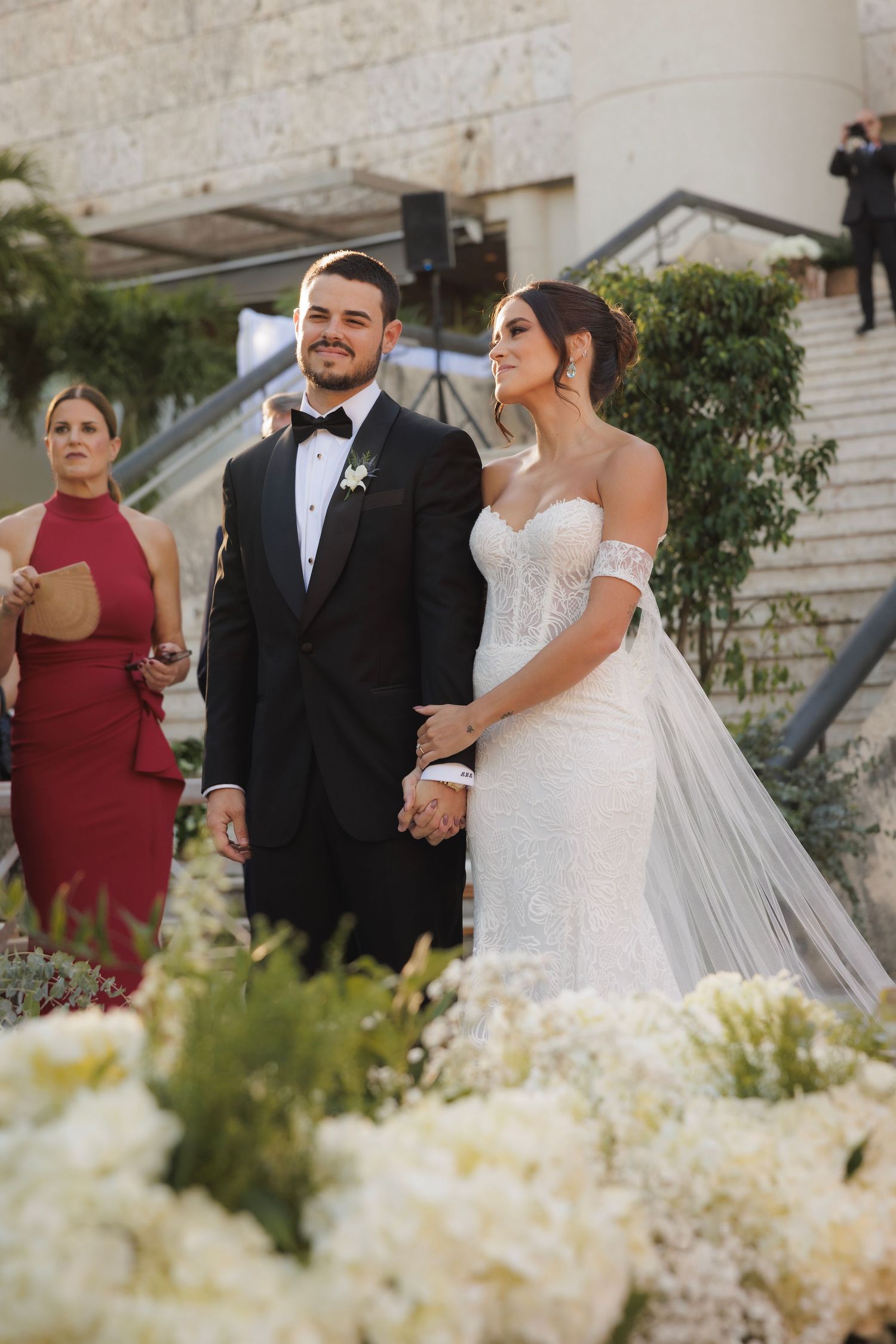Wedding ceremony outdoors with white floral arrangements and stone backdrop.