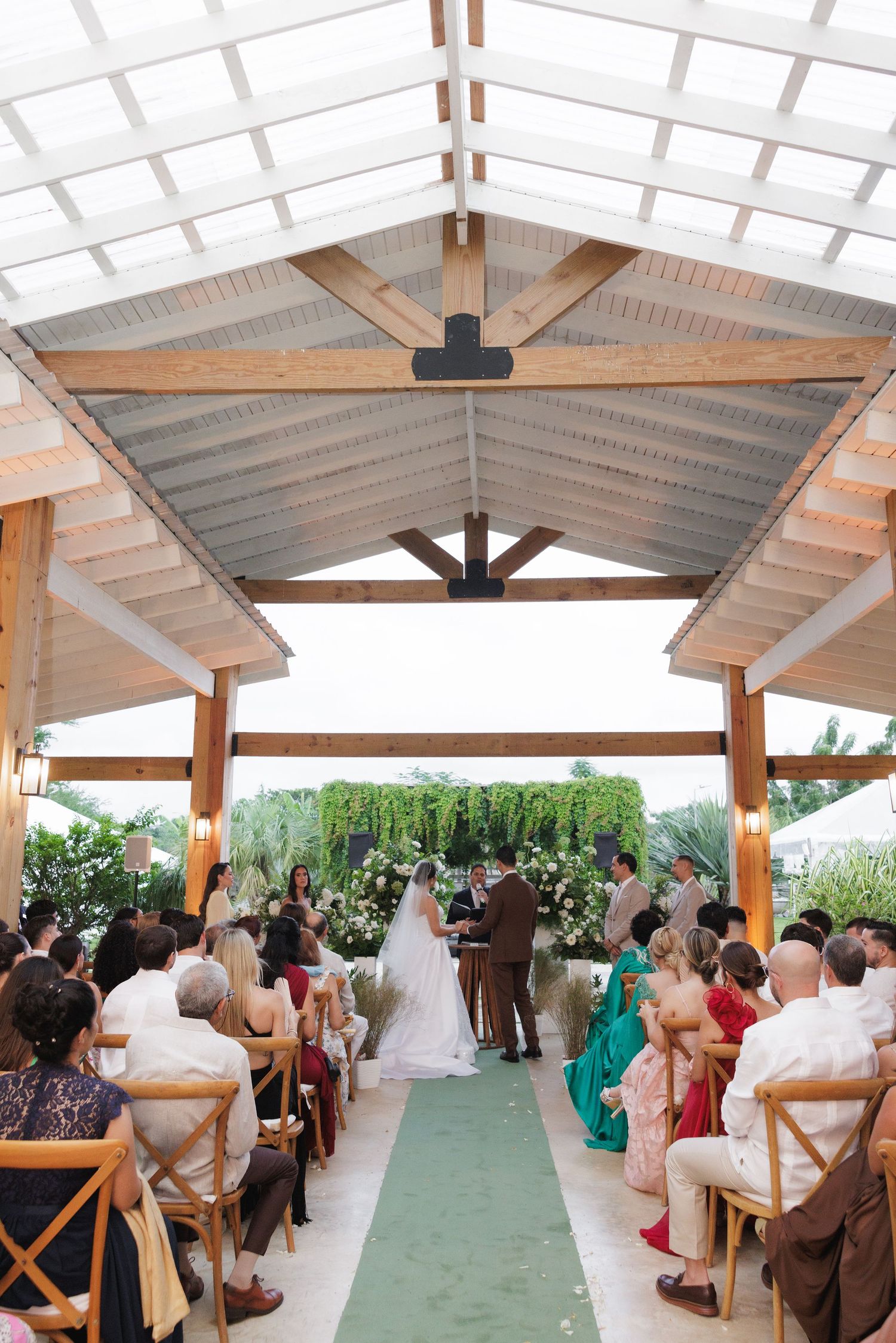 Panoramic view of a covered outdoor wedding venue with green aisle runner and wooden beams.